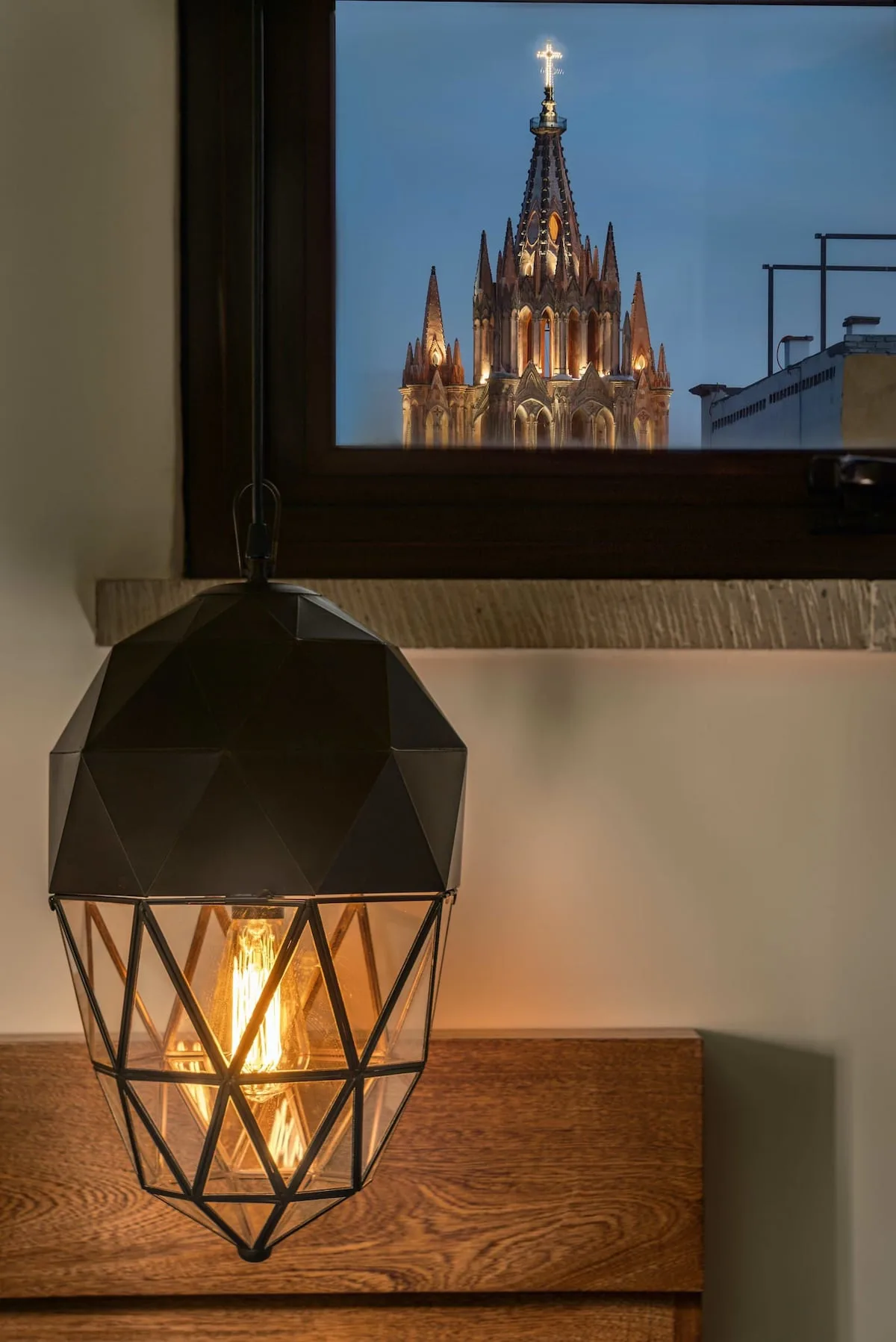 A glowing geometric lamp sits beneath a window overlooking an illuminated cathedral.