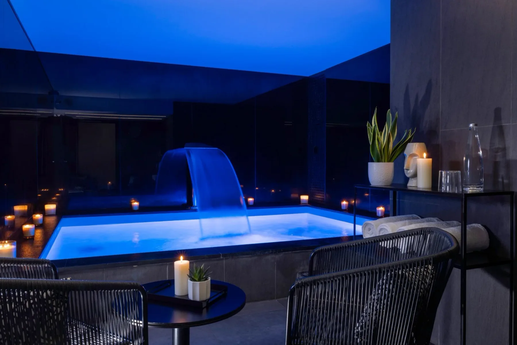 Representative hotel space: A blue-lit indoor pool sits beside dark lounge seating and small tables.