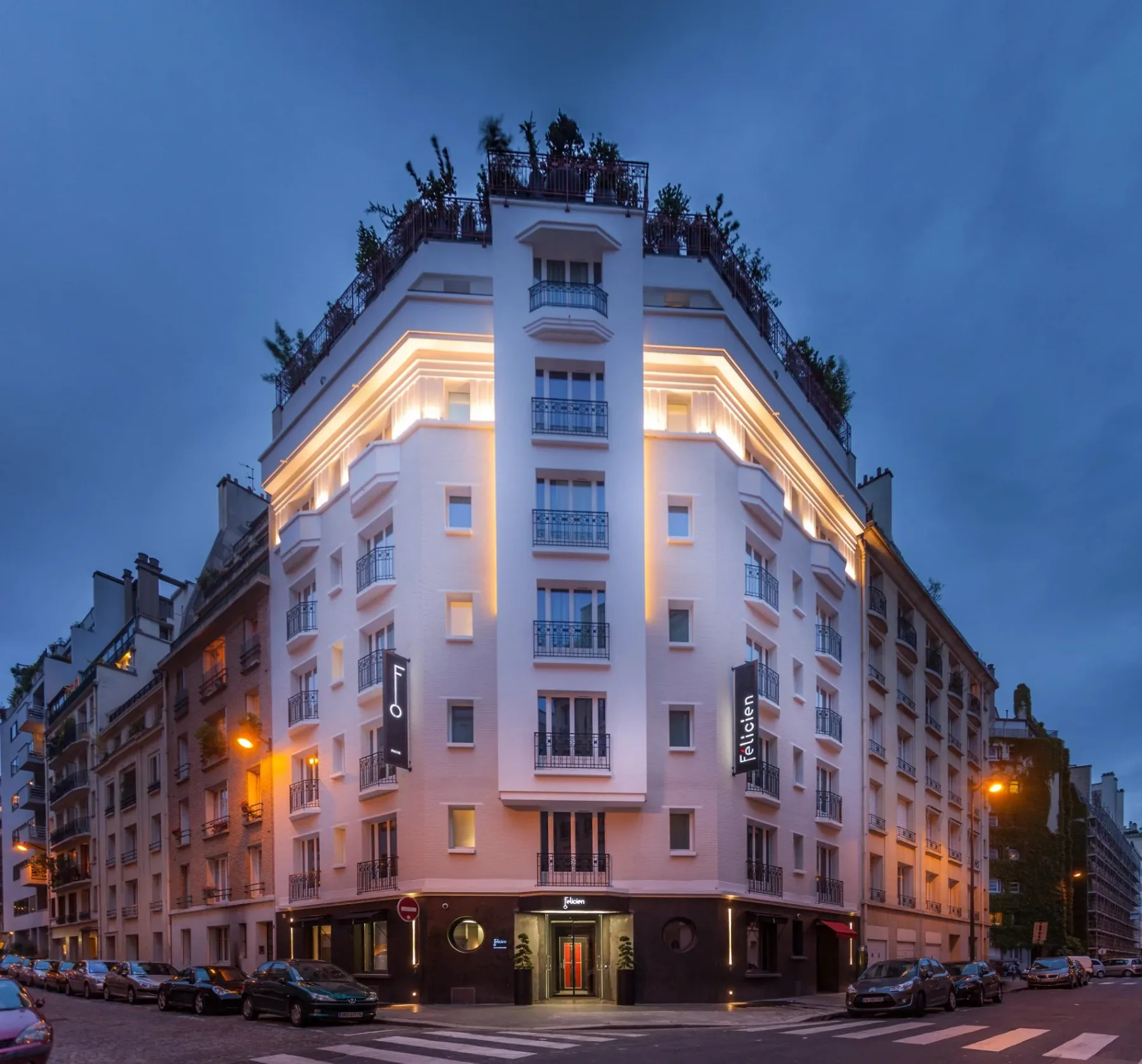 Representative hotel space: A brightly lit corner hotel building stands along a city street at dusk.