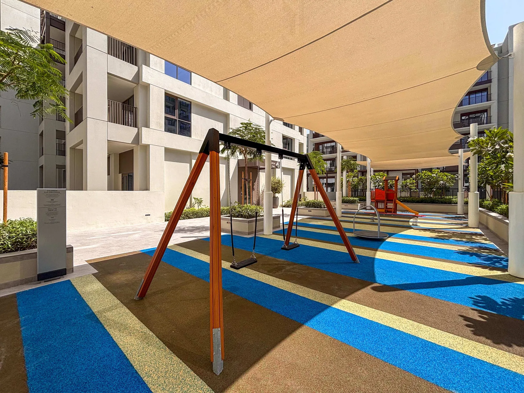 Shared amenity: Outdoor playground with a swing set beneath a large shade canopy.