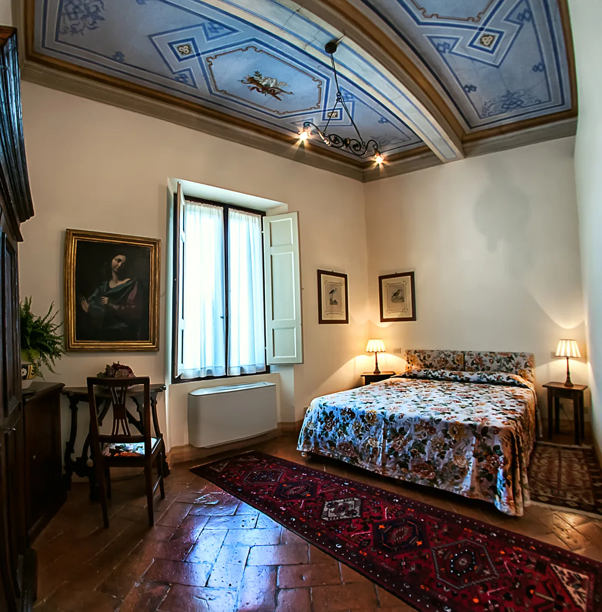 Espacio representativo del hotel: Un dormitorio con una colcha floral, una ventana y un techo pintado.