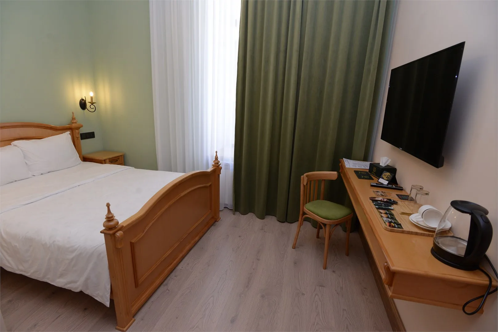 Espacio representativo del hotel: Dormitorio con cama de madera, escritorio y televisor montado en la pared.