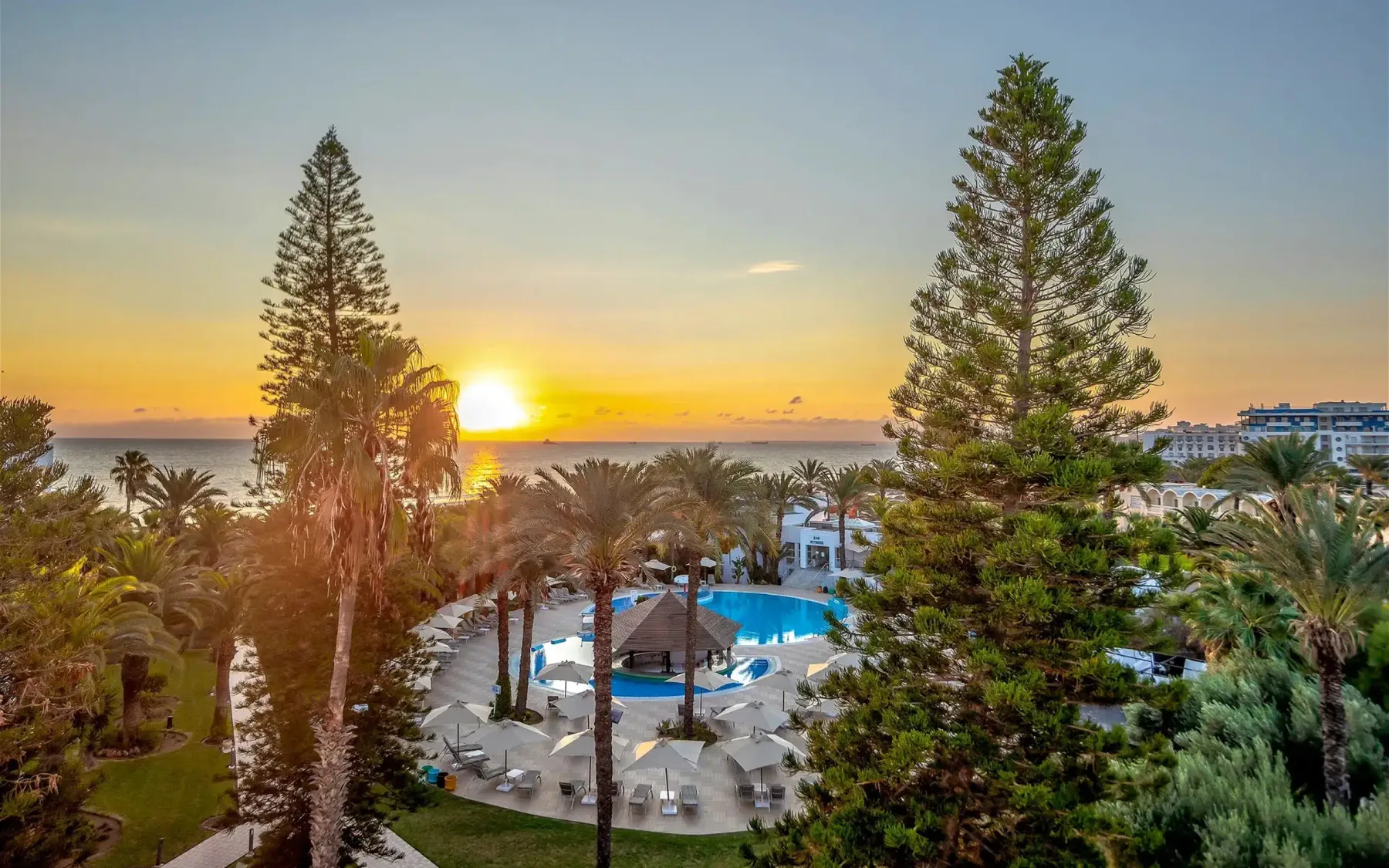 Espacio representativo del hotel: Una piscina y un jardín del complejo turístico miran al mar al atardecer.