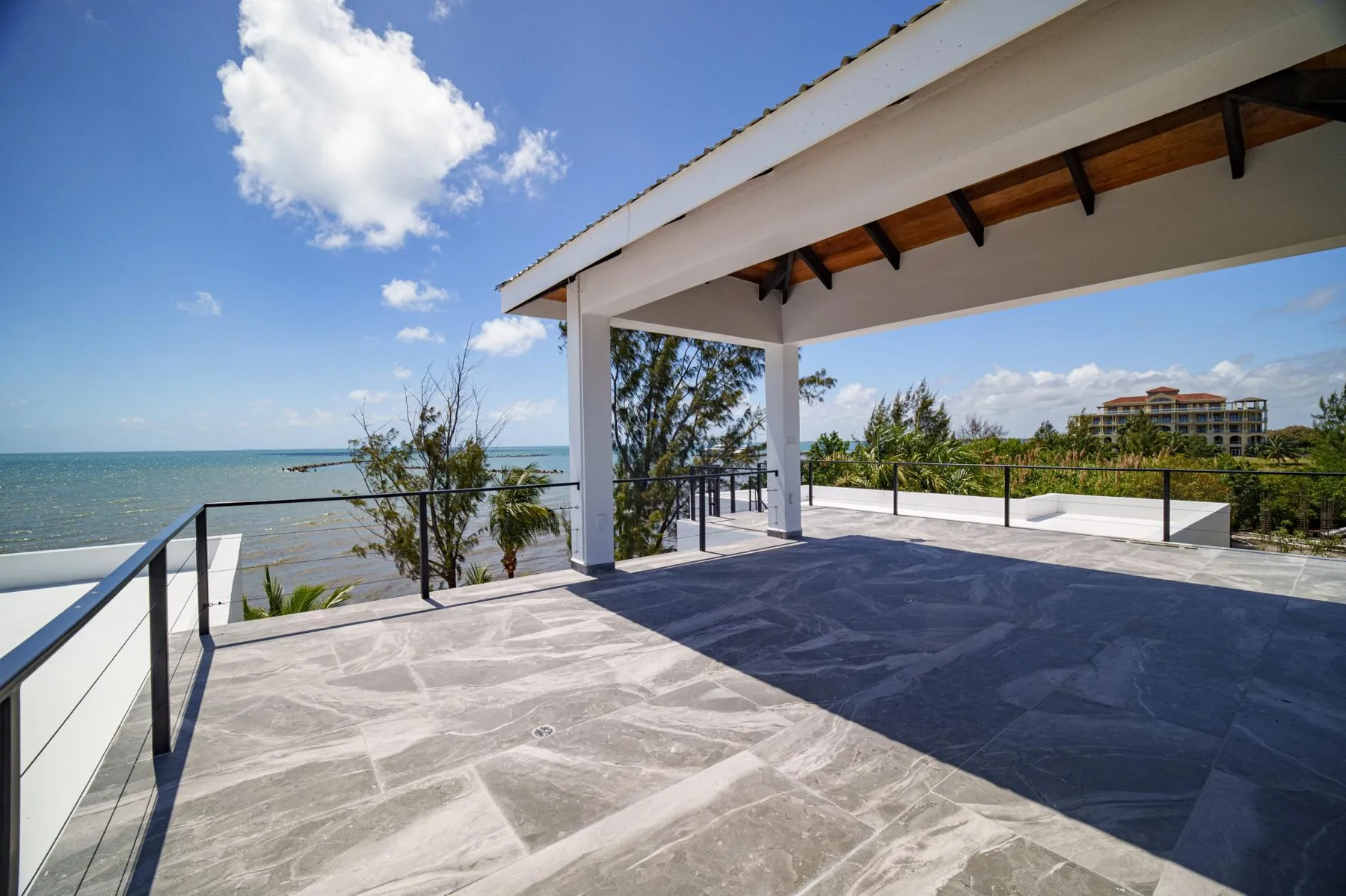 A covered outdoor terrace overlooks the water, with open sky and greenery beyond.