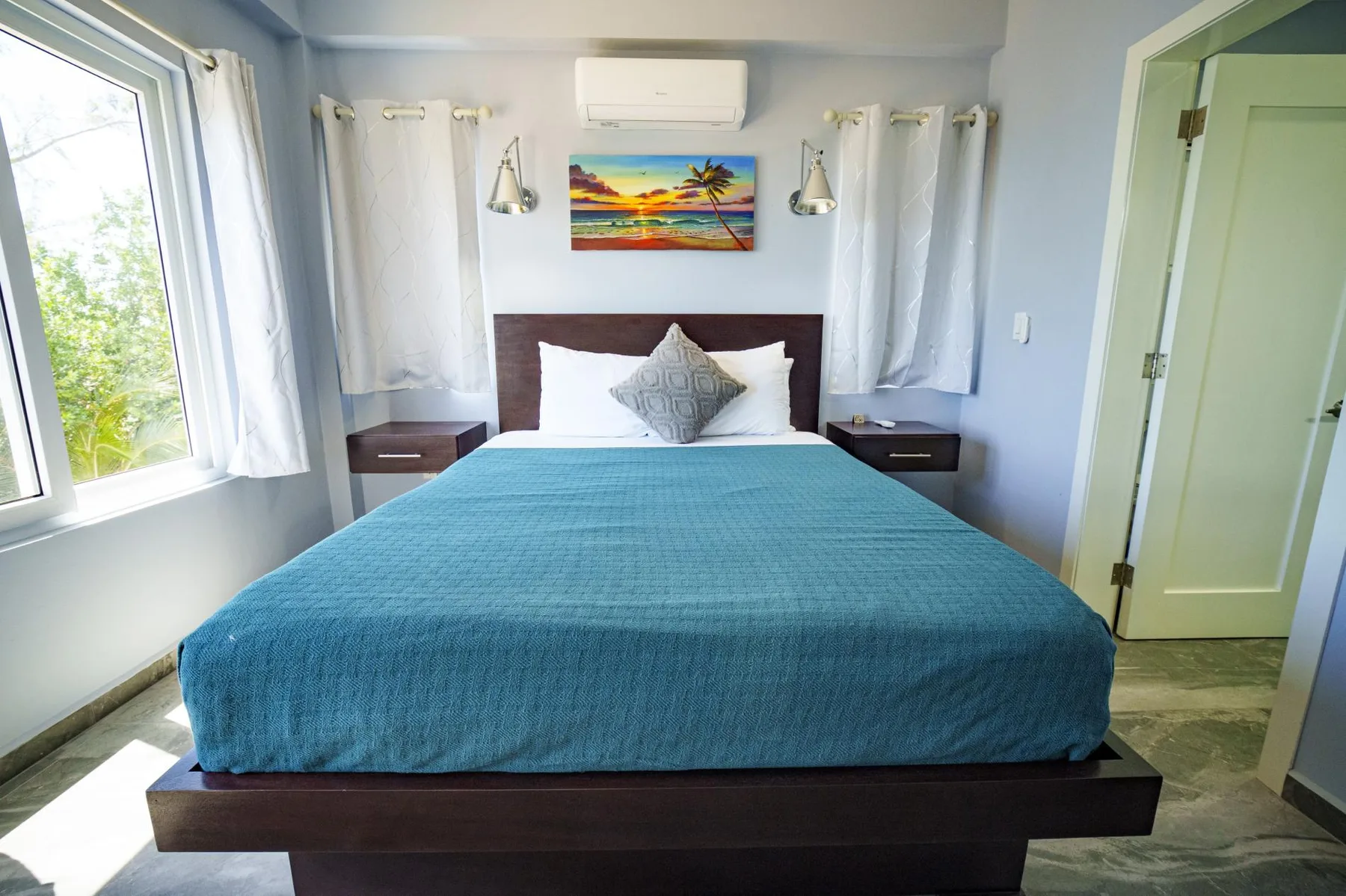 A bedroom with a bed covered in a teal bedspread beneath a colorful wall picture.