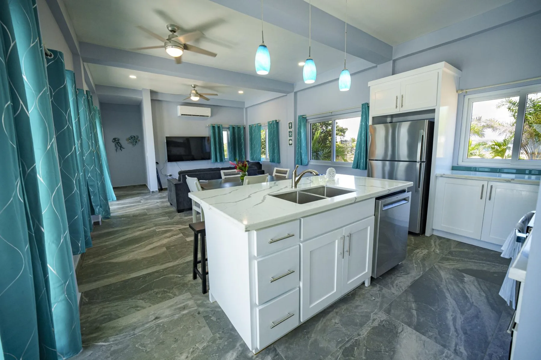 A bright kitchen with a white island, stainless steel appliances, and teal curtains.