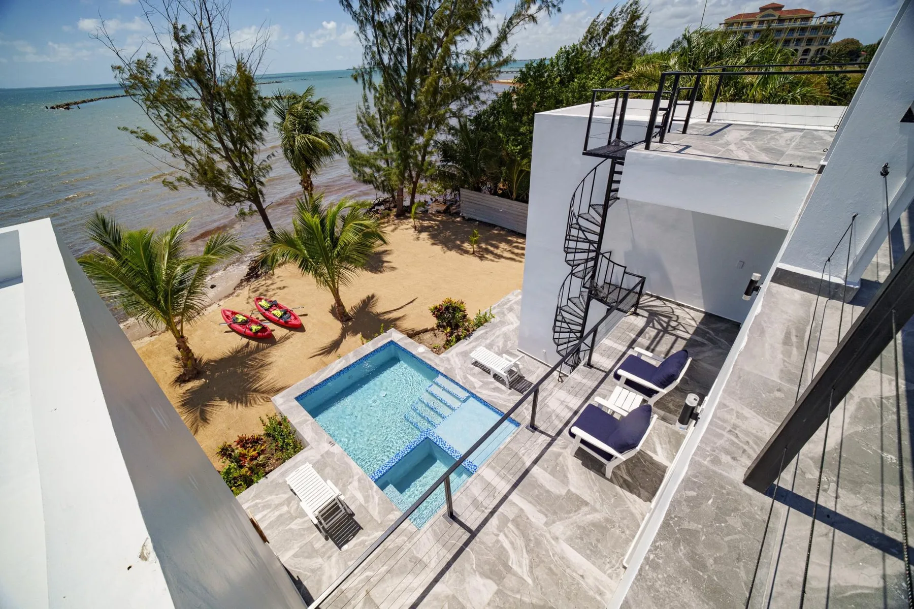 A seaside pool deck overlooks a sandy beach and turquoise water.