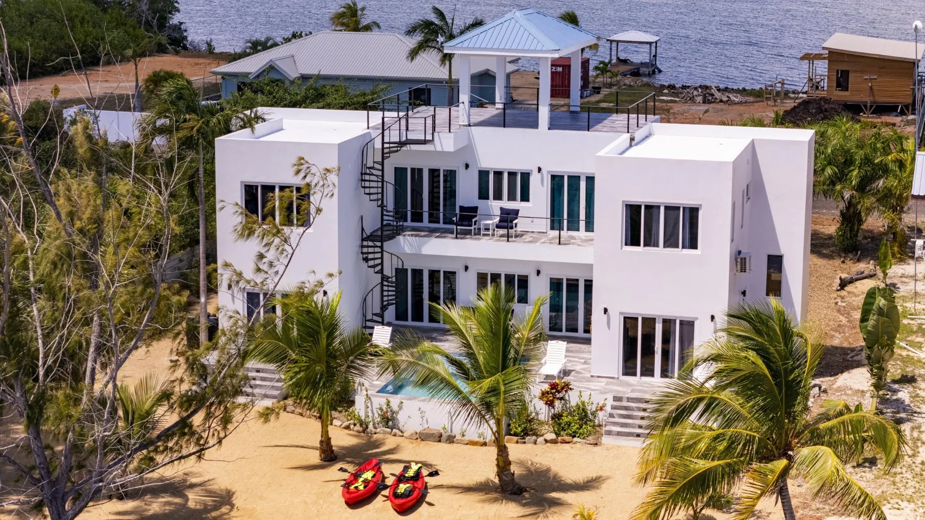 A modern white house stands beside a sandy shoreline, with a small pool in front.