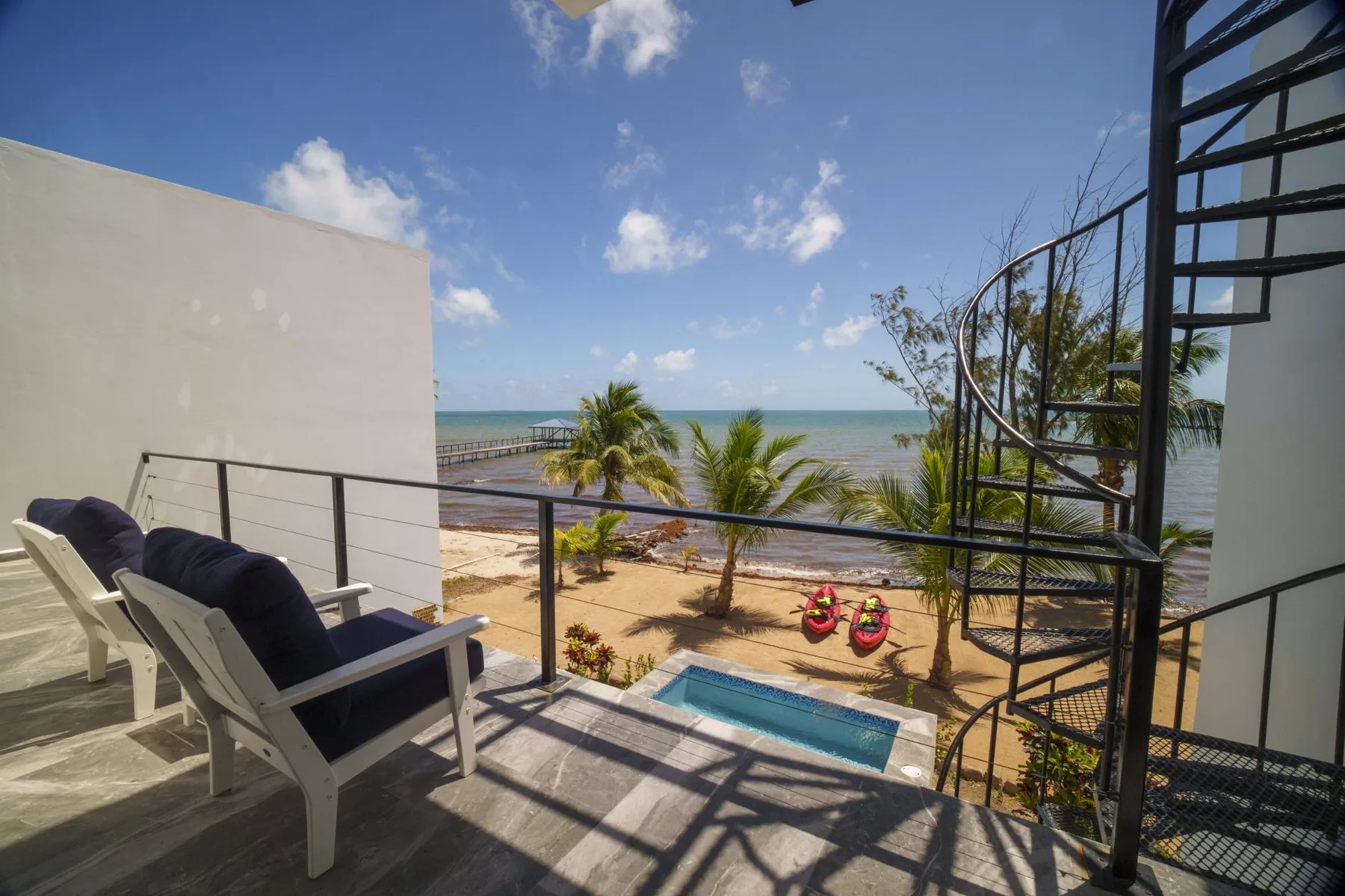 A terrace overlooks a small pool, palm trees, and the ocean.