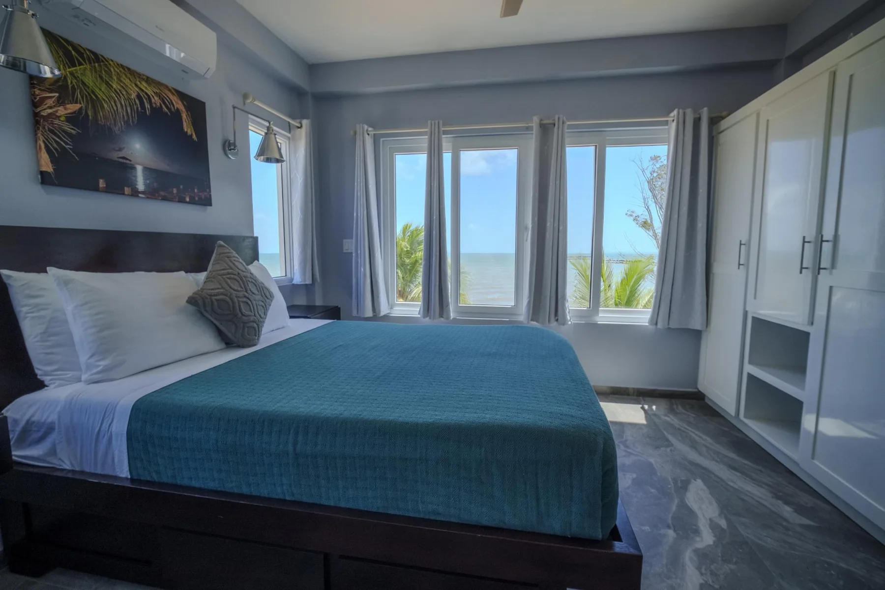A bedroom with a bed beside windows overlooking the sea.