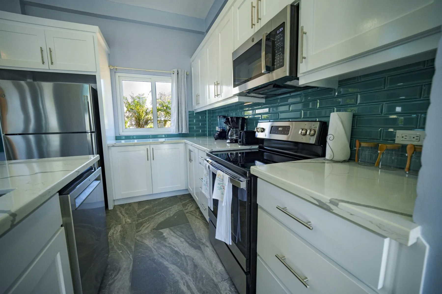 A bright kitchen with white cabinets, stainless steel appliances, and a dark tiled backsplash.