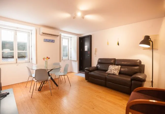 A living and dining area with a dark sofa and a table beside the windows.