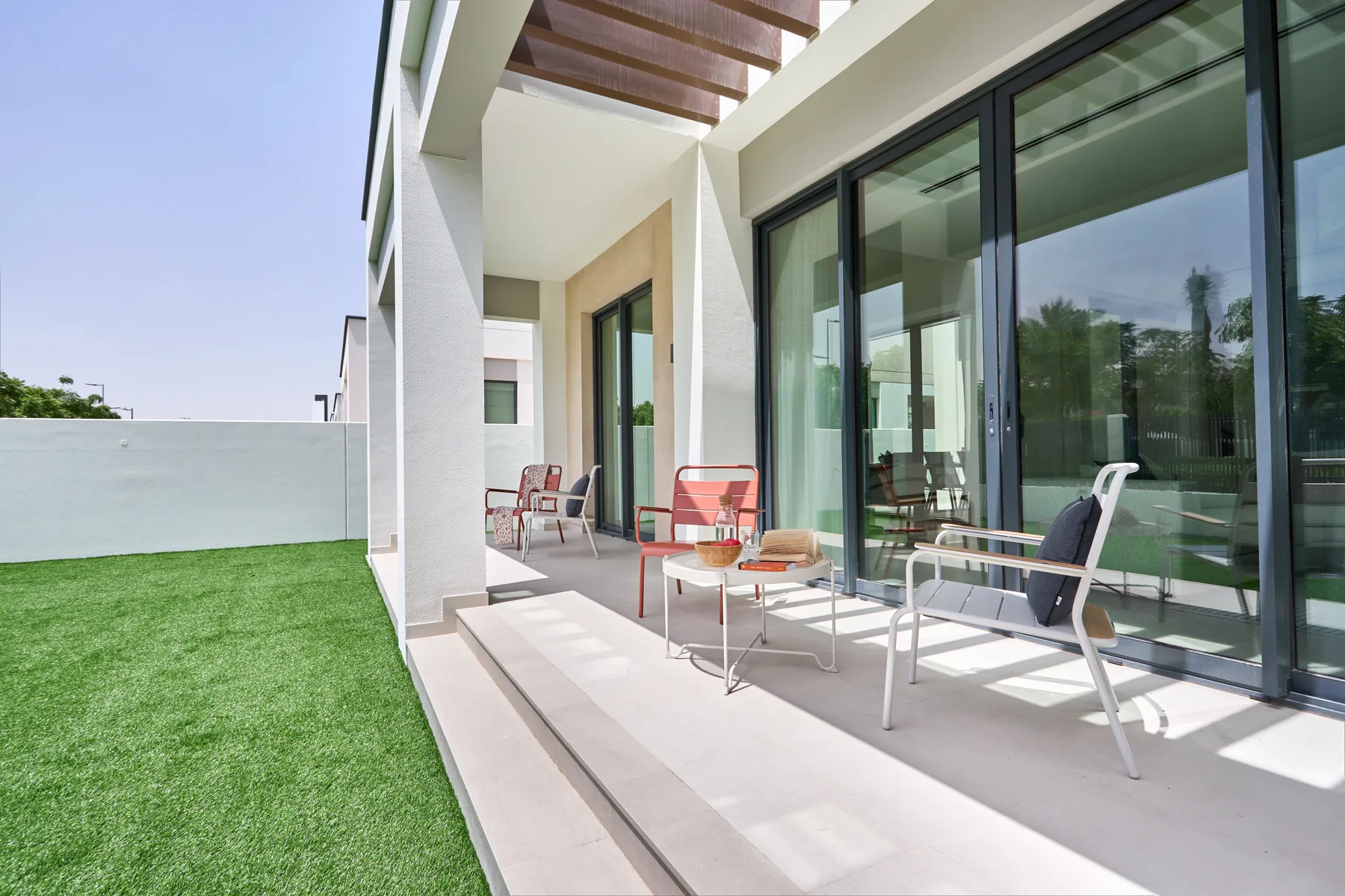 Un patio moderno con asientos exteriores junto a grandes puertas de vidrio y un césped.