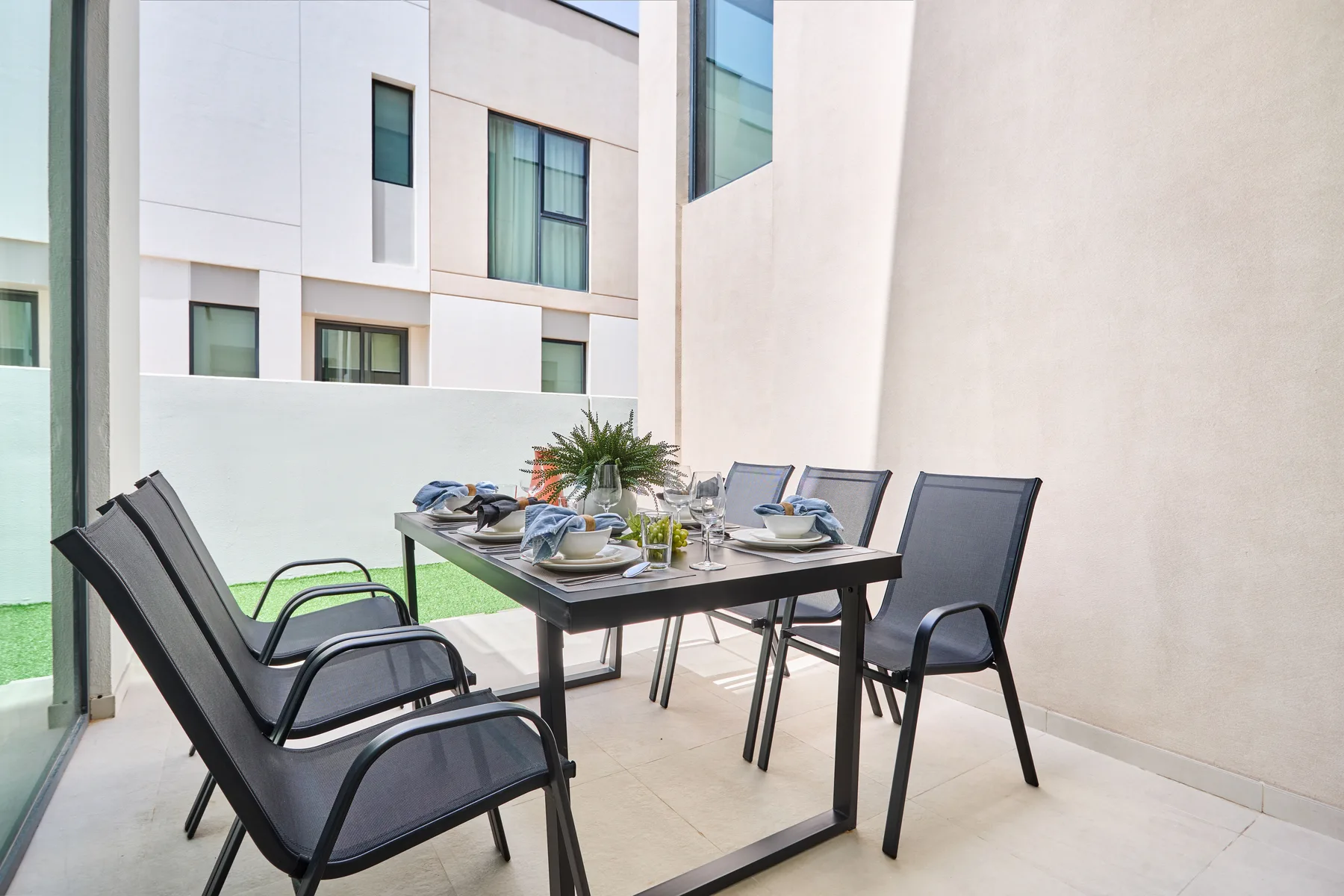 Un comedor al aire libre con una mesa puesta, sillas negras y una planta en maceta.