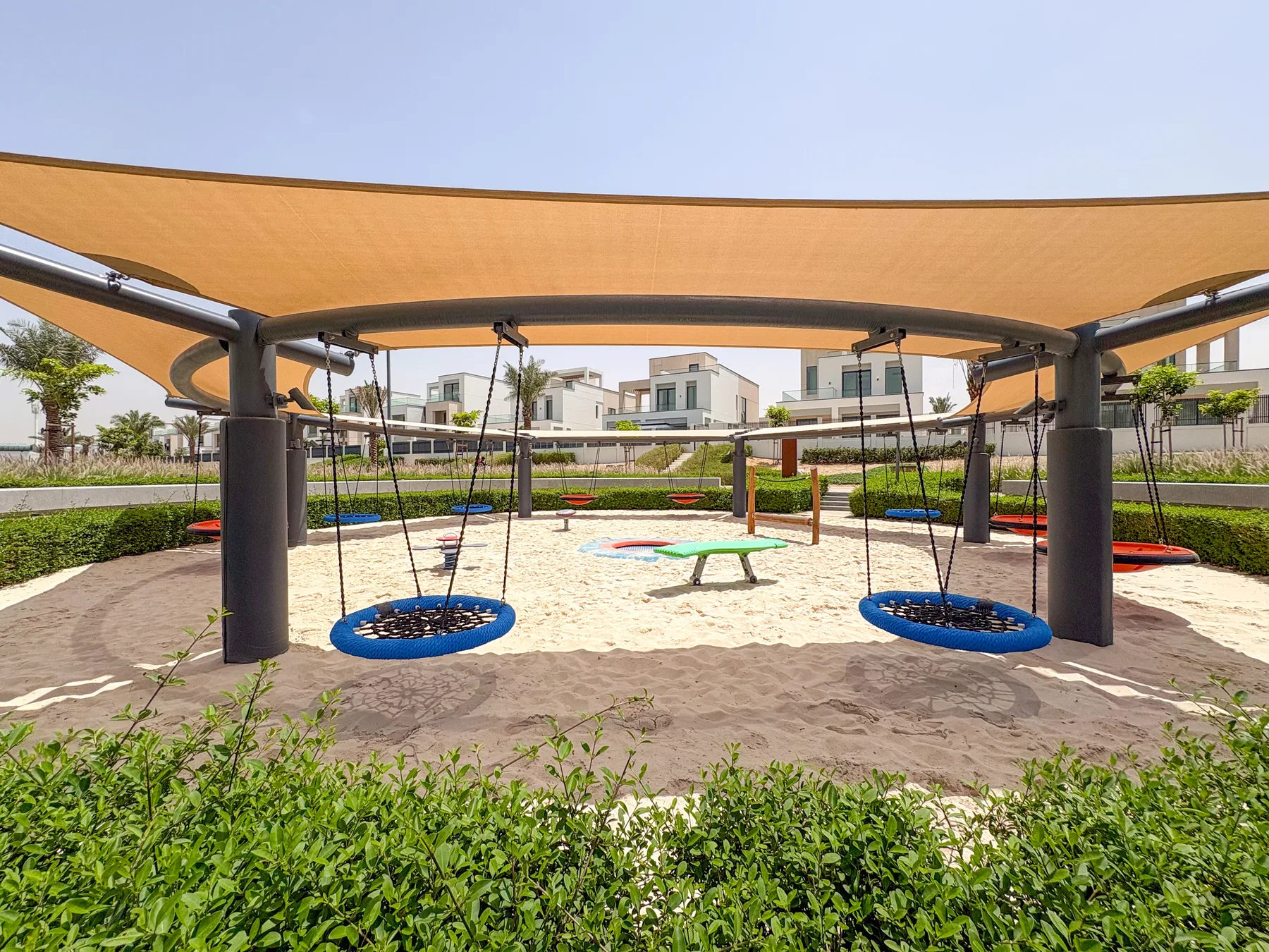 Zona común: Un parque infantil con columpios y un pequeño carrusel bajo una cubierta de sombra.