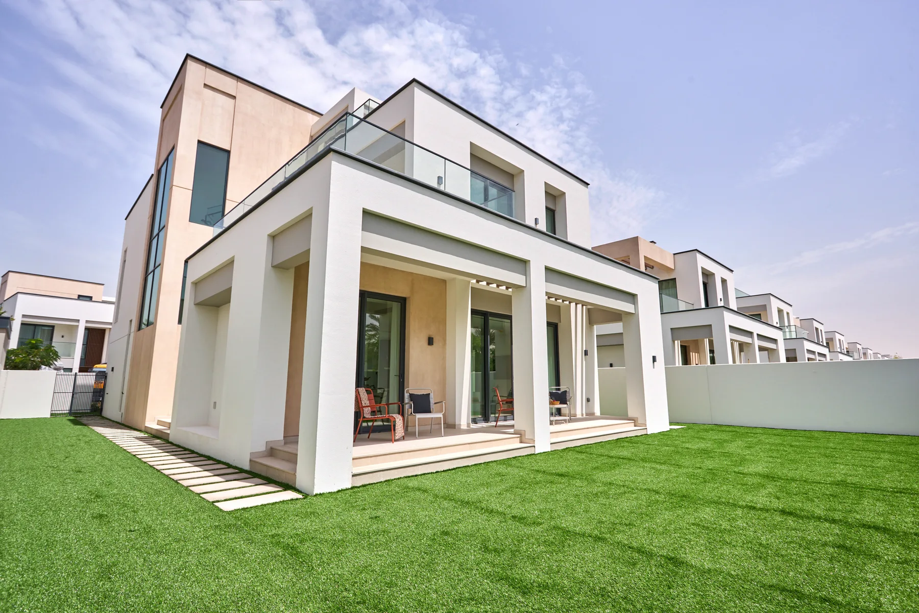 Una casa moderna blanca con grandes ventanas se alza junto a un césped verde.