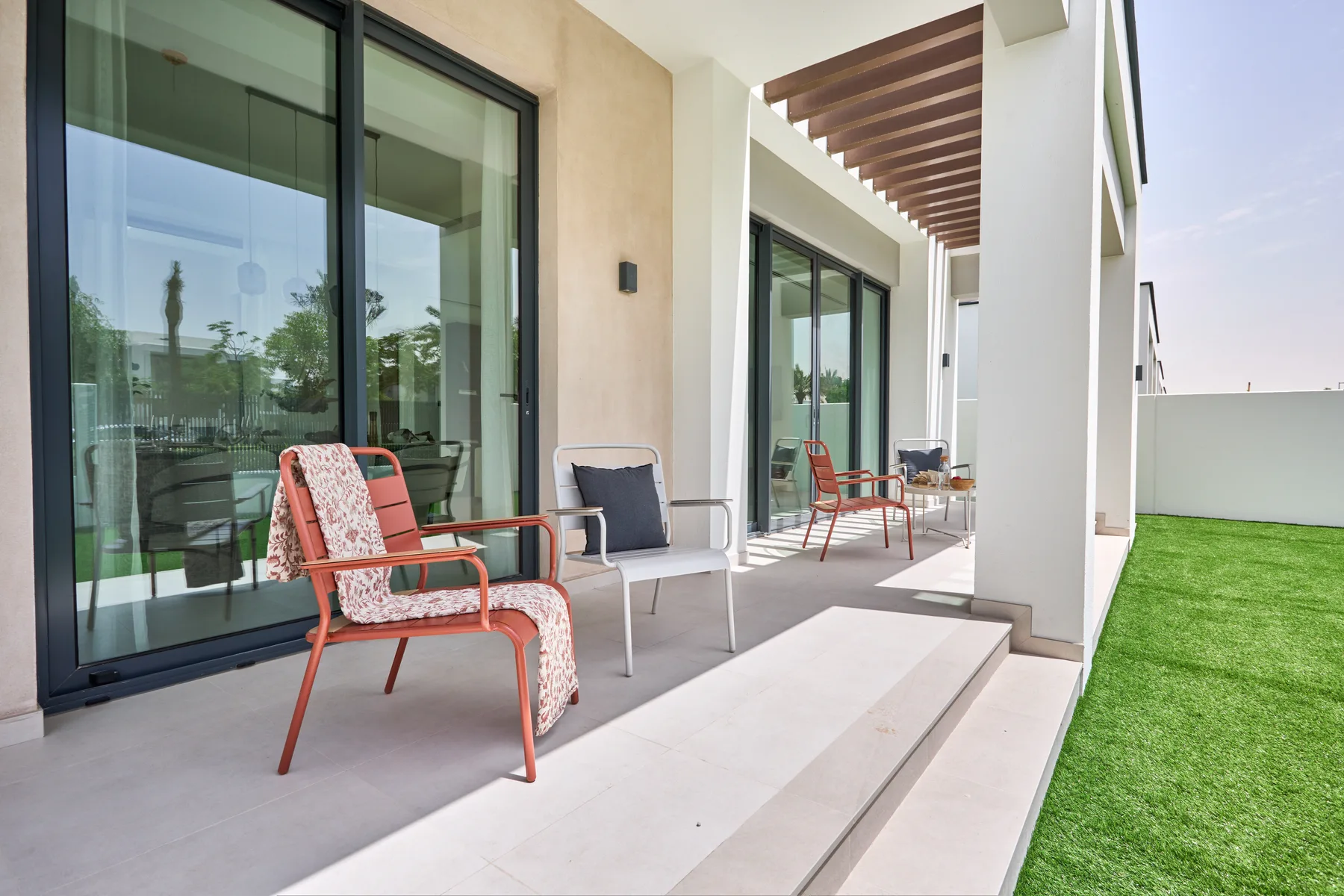 Un patio cubierto con asientos al aire libre junto a puertas corredizas de vidrio y un césped.