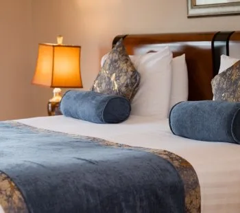 Representative hotel space: A bedroom with a neatly made bed and a lit bedside lamp.