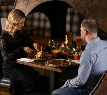 Representative hotel space: A couple shares a meal at a table beside a lit fireplace.