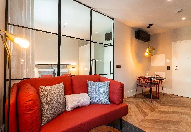 Una sala de estar con asientos rojos y un tabique de vidrio junto a una mesa de comedor.