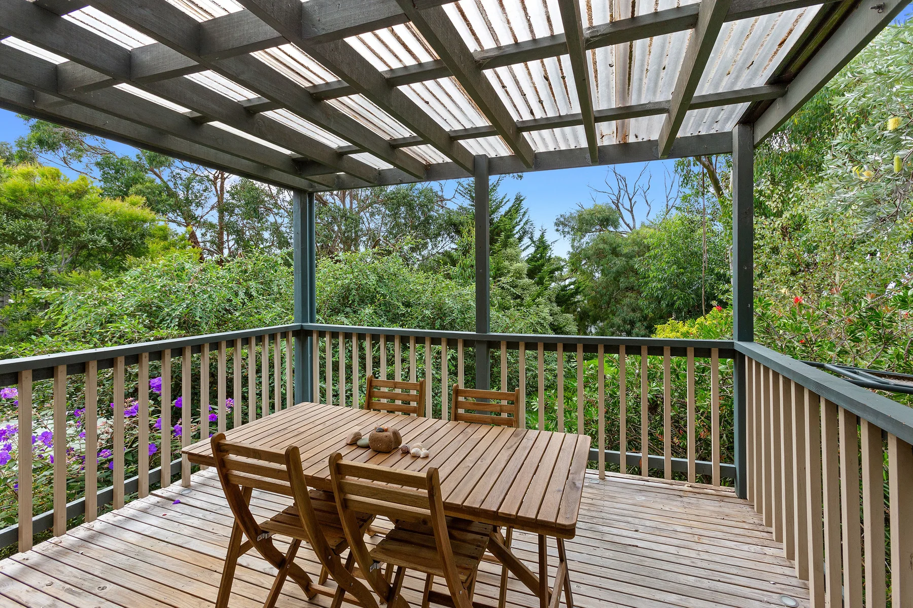 Una terraza exterior cubierta con una mesa de comedor de madera rodeada de vegetación.