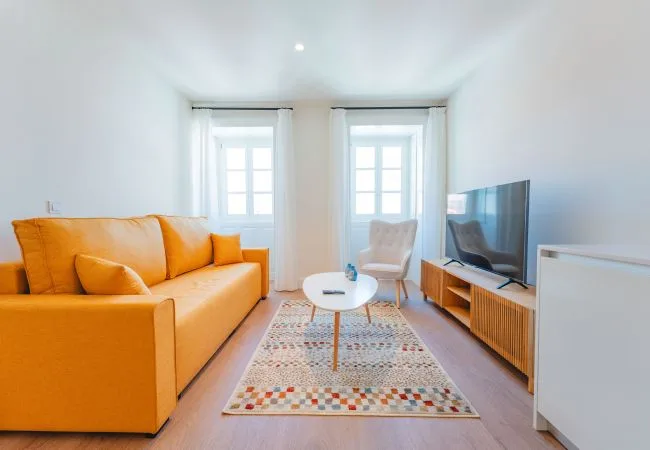 Una sala luminosa con asientos naranjas, un televisor y una alfombra estampada.