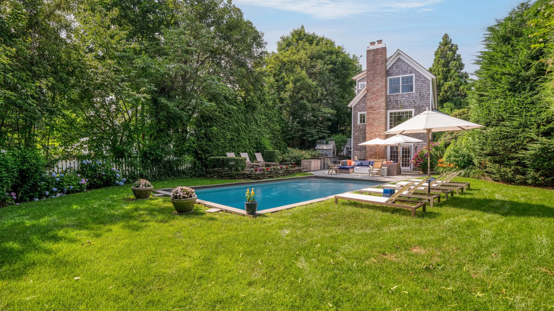 An outdoor swimming pool and lawn sit beside a house, surrounded by trees.