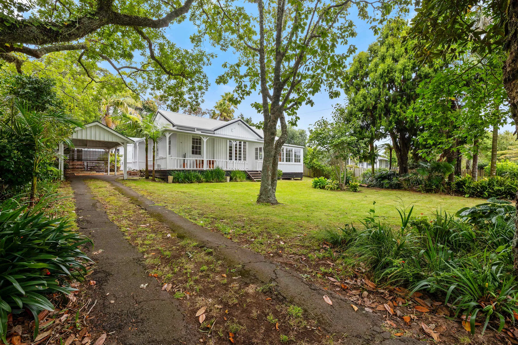 Una pequeña casa blanca está junto a un patio arbolado y un sendero.