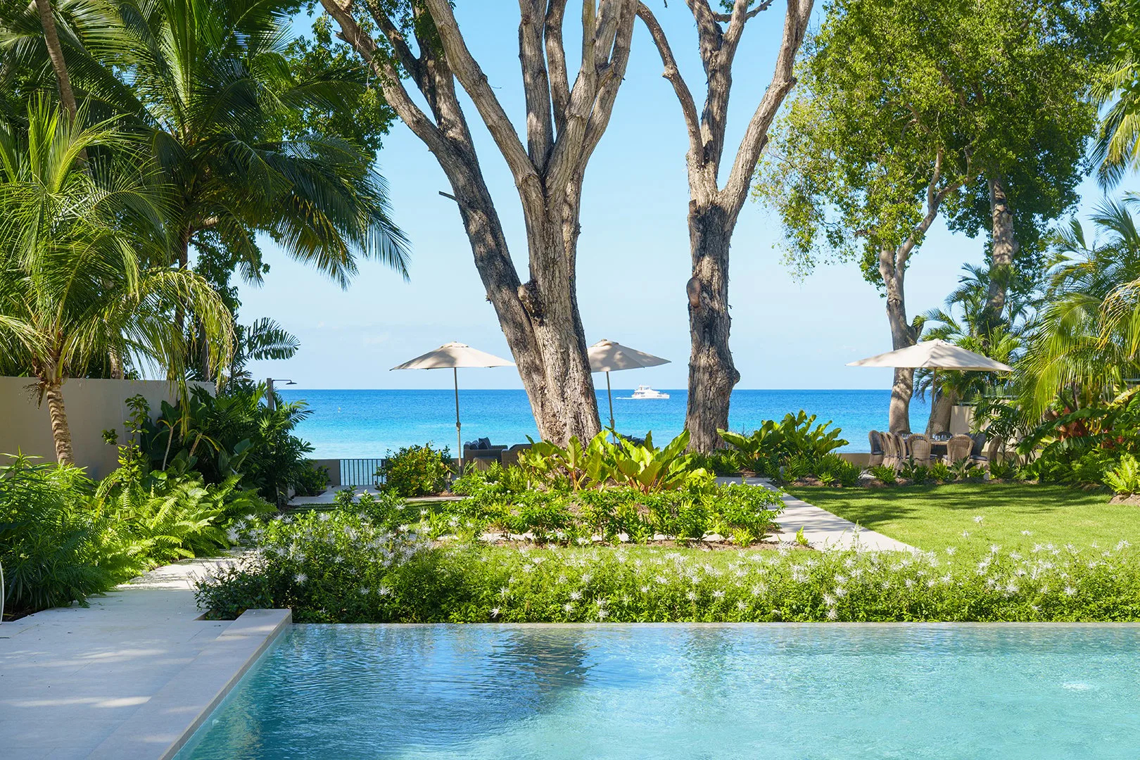 A swimming pool overlooks a landscaped garden and the ocean.