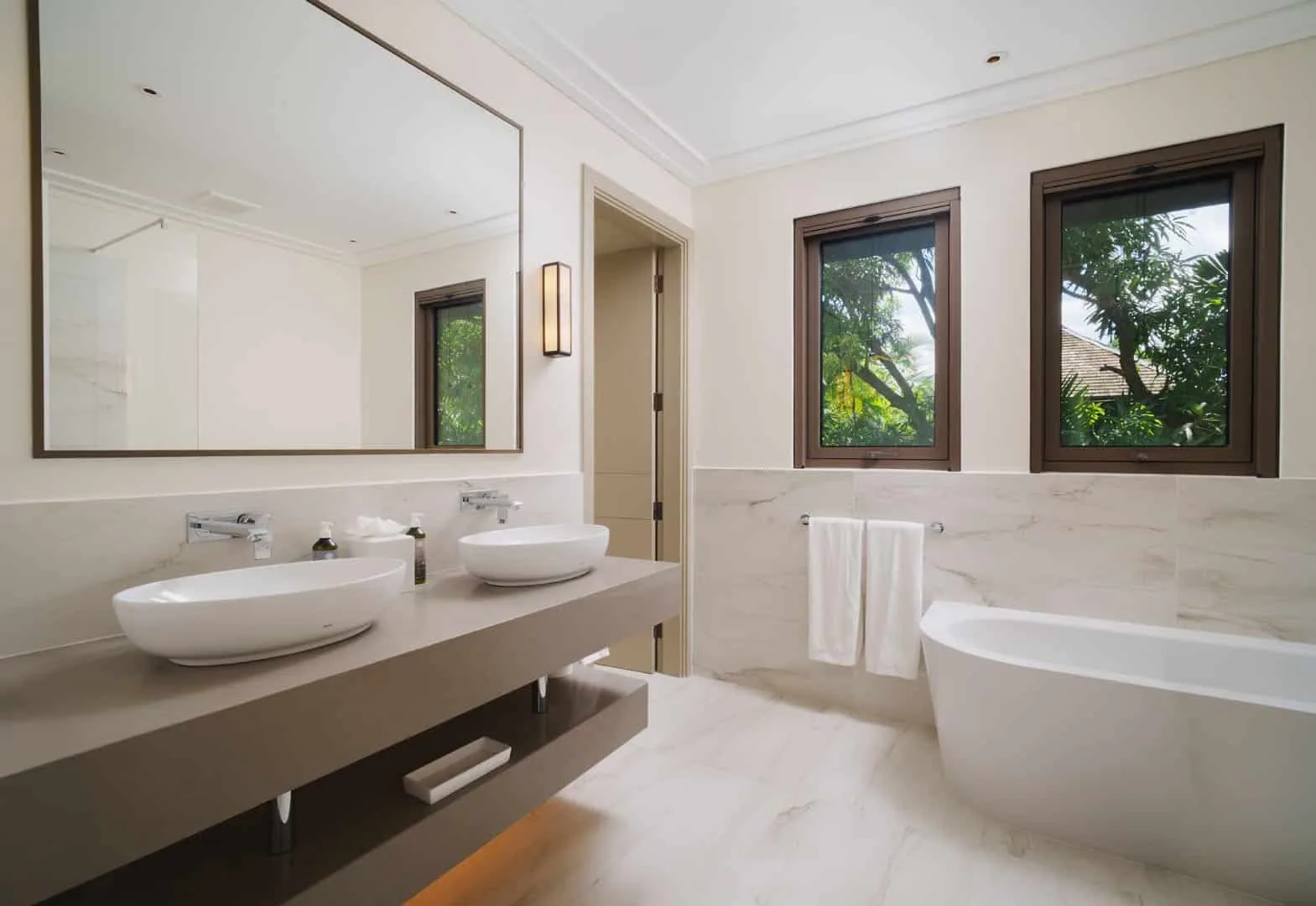 A bright bathroom with two sinks, a large mirror, and a bathtub.