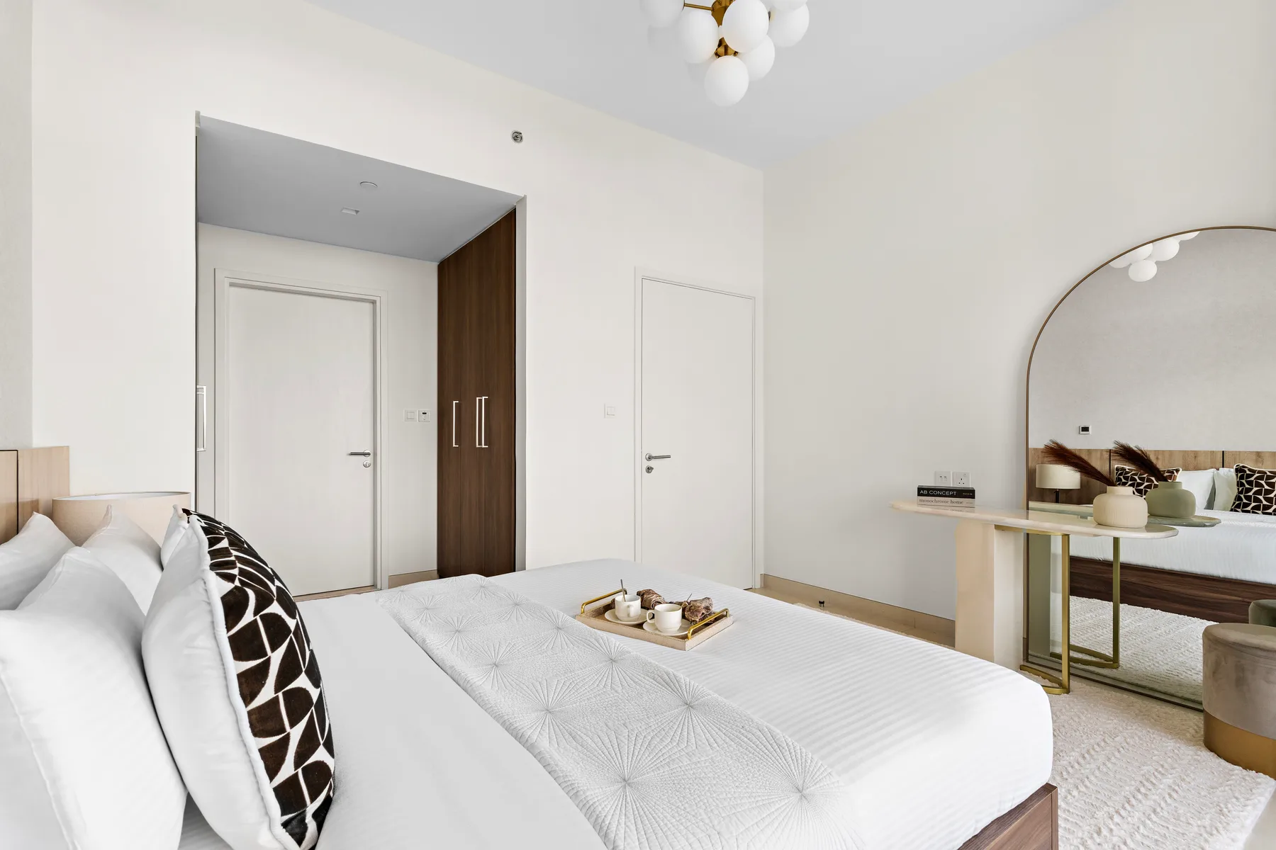 A bright bedroom with a neatly made bed and a large arched mirror.