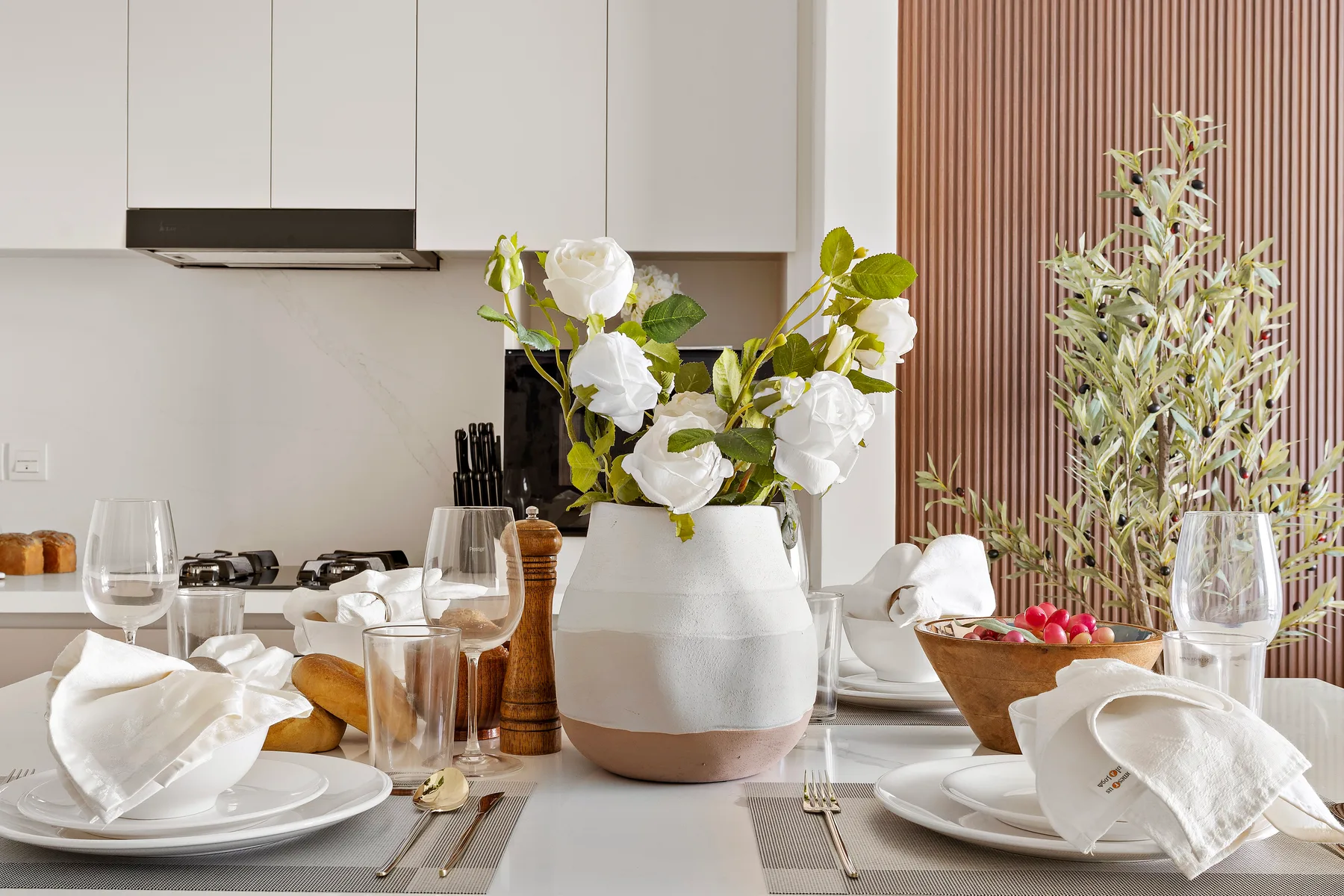 A dining table is set with plates, glassware, and a vase of white flowers.