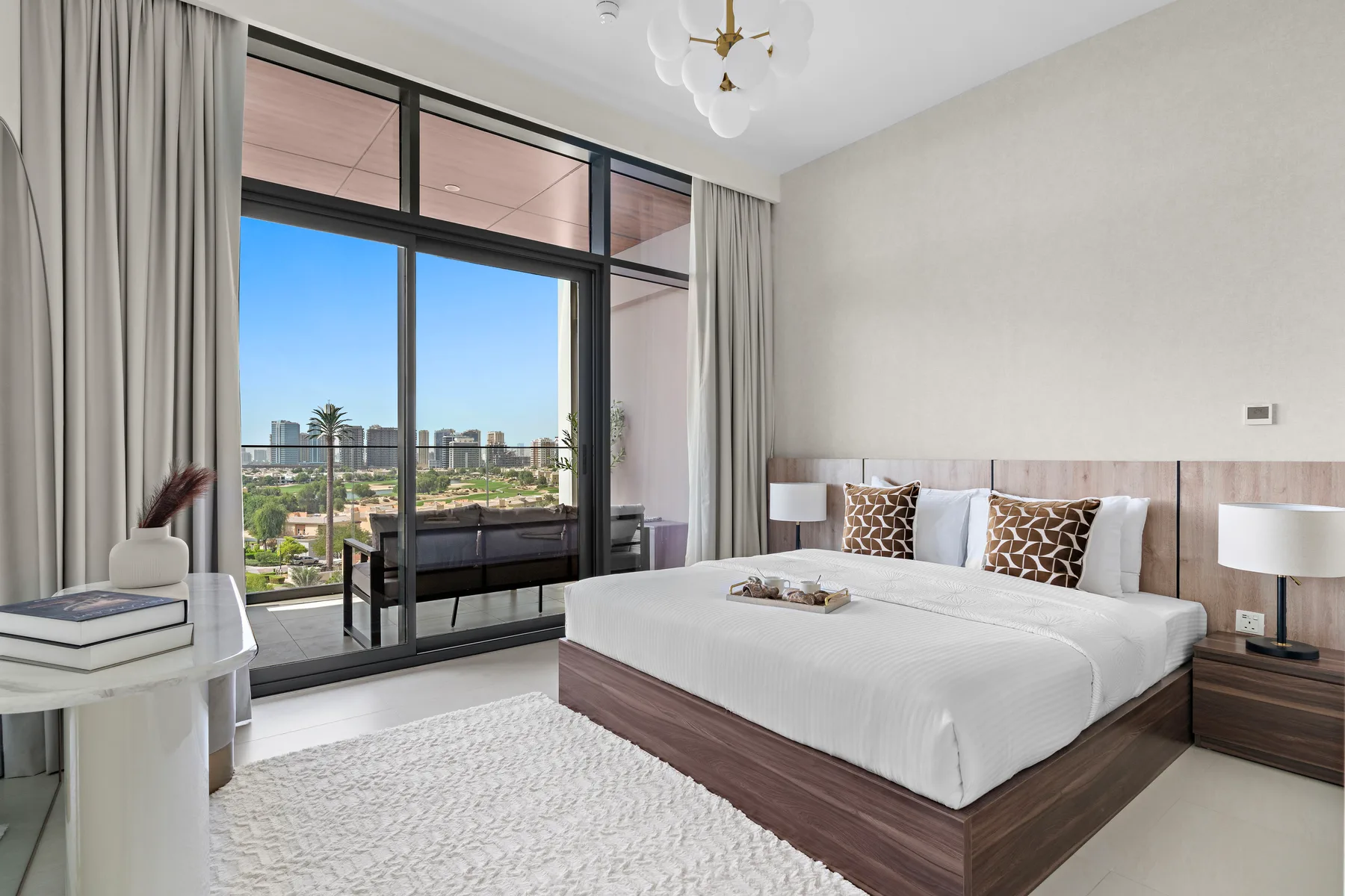 A bright bedroom with a large bed beside floor-to-ceiling windows.