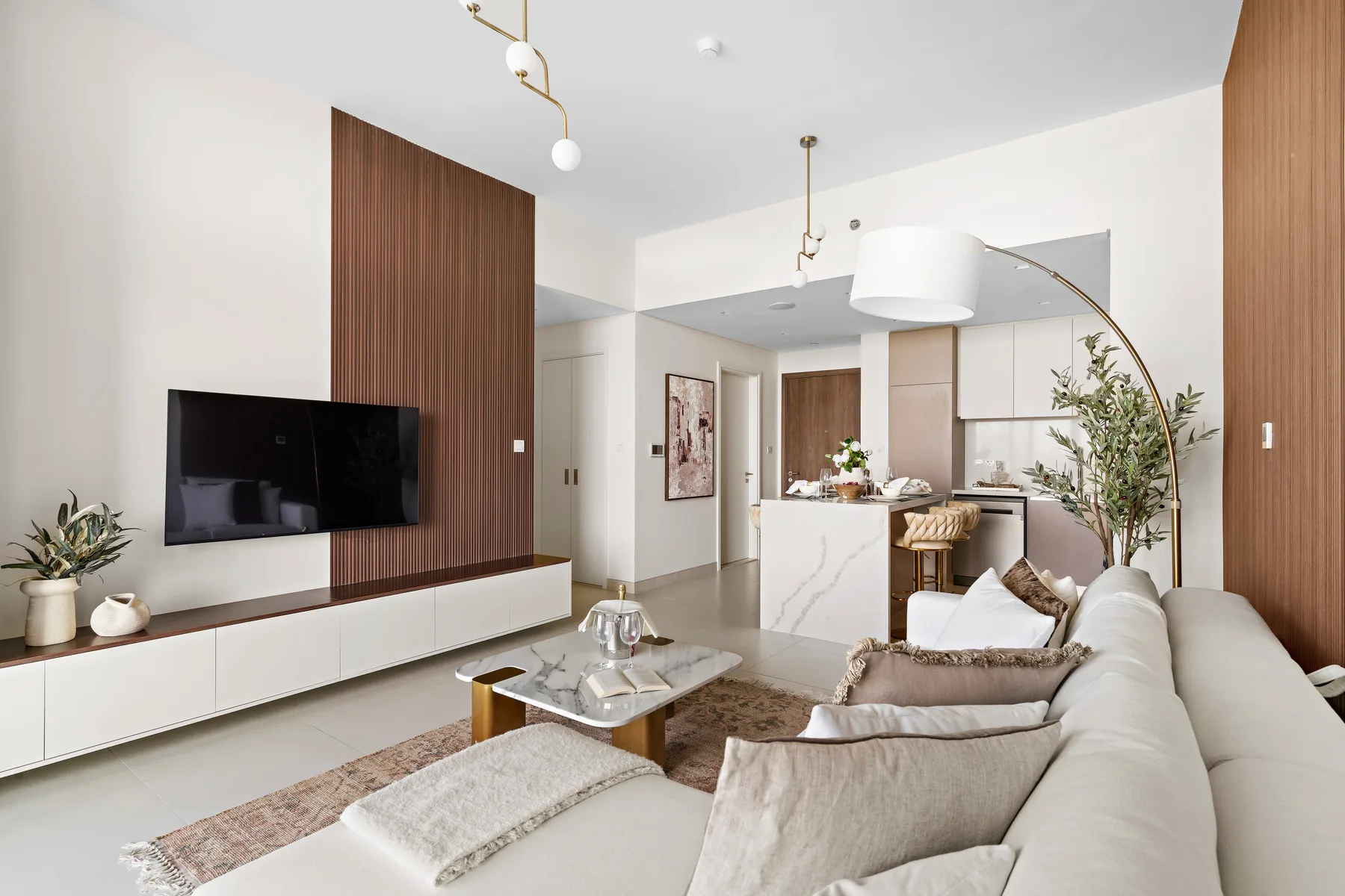 A modern living room with pale seating, a television, and an open kitchen.