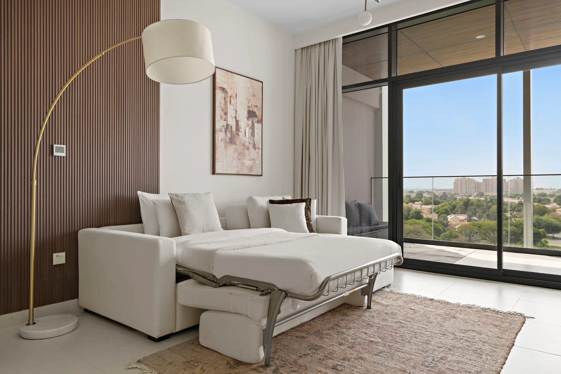 A bright living area with a sofa bed beside large windows overlooking greenery.