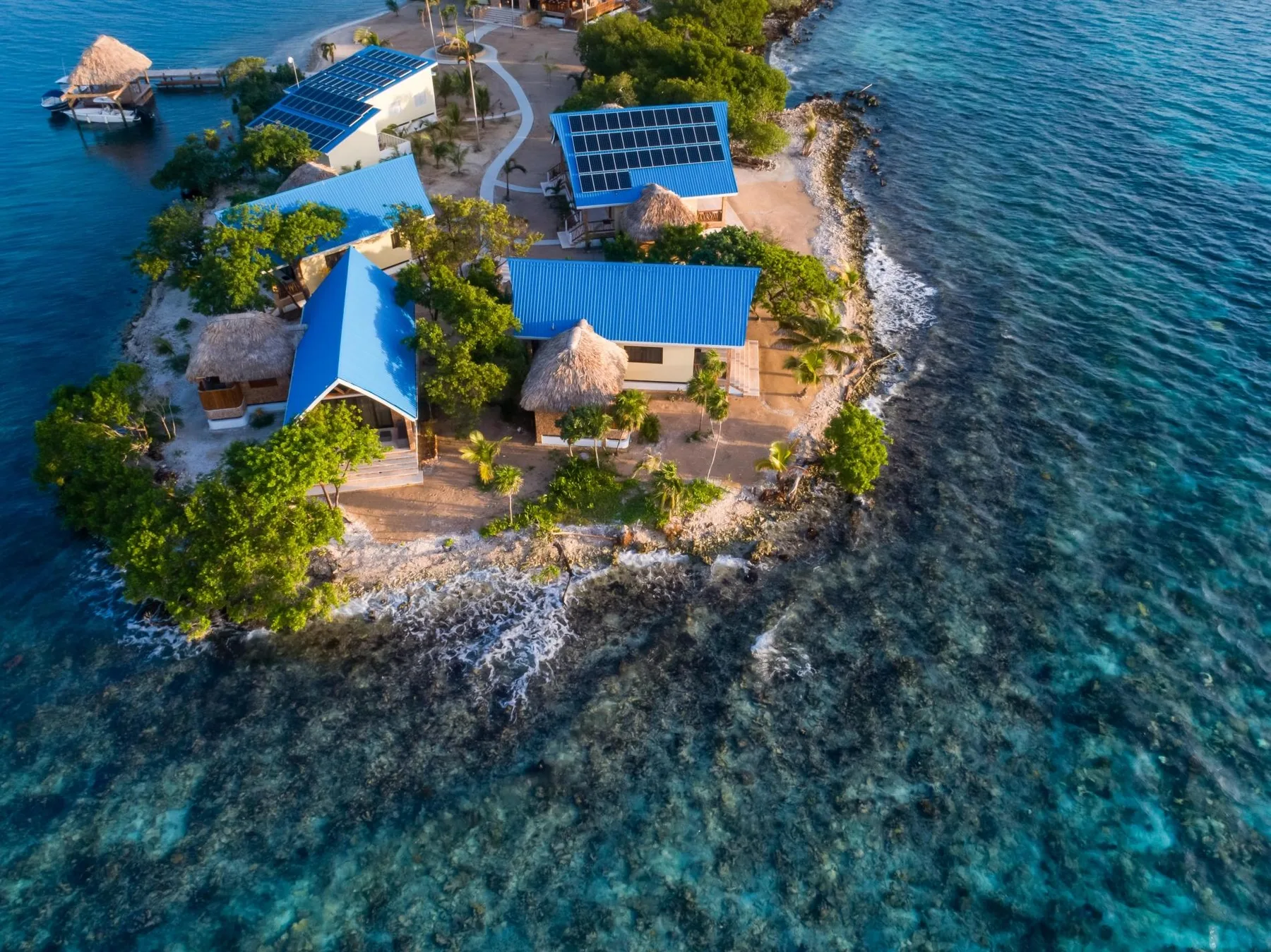 An aerial view of a small coastal settlement with blue-roofed buildings beside clear water.