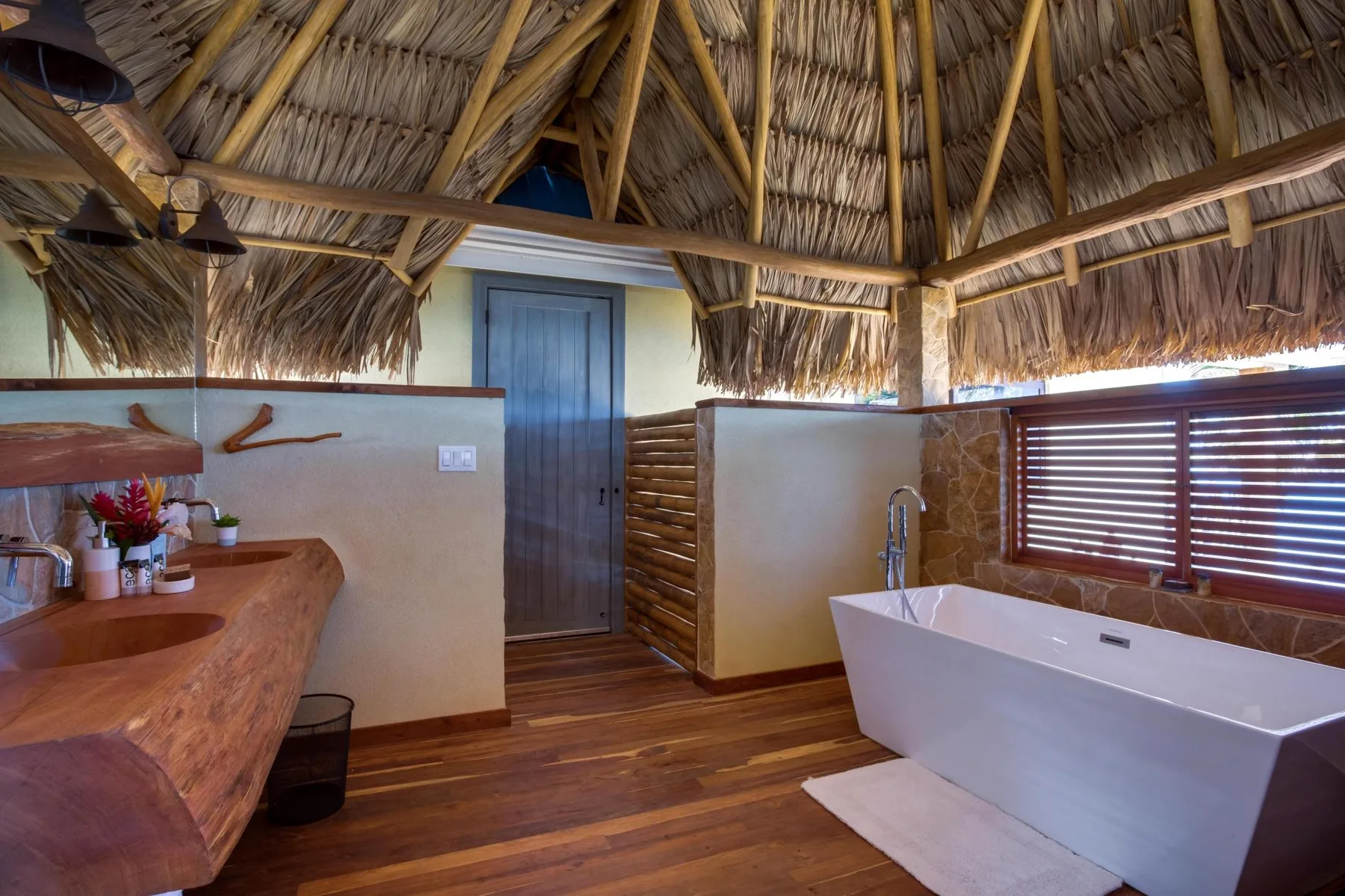 A bathroom with a freestanding bathtub beneath a thatched roof.