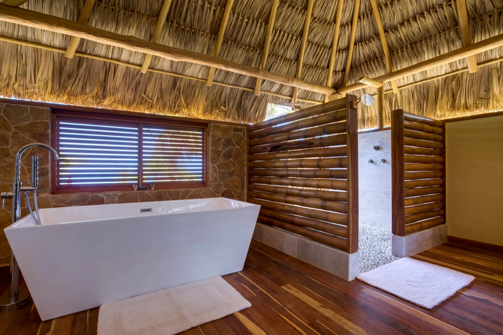 A rustic bathroom with a freestanding bathtub and a thatched ceiling.