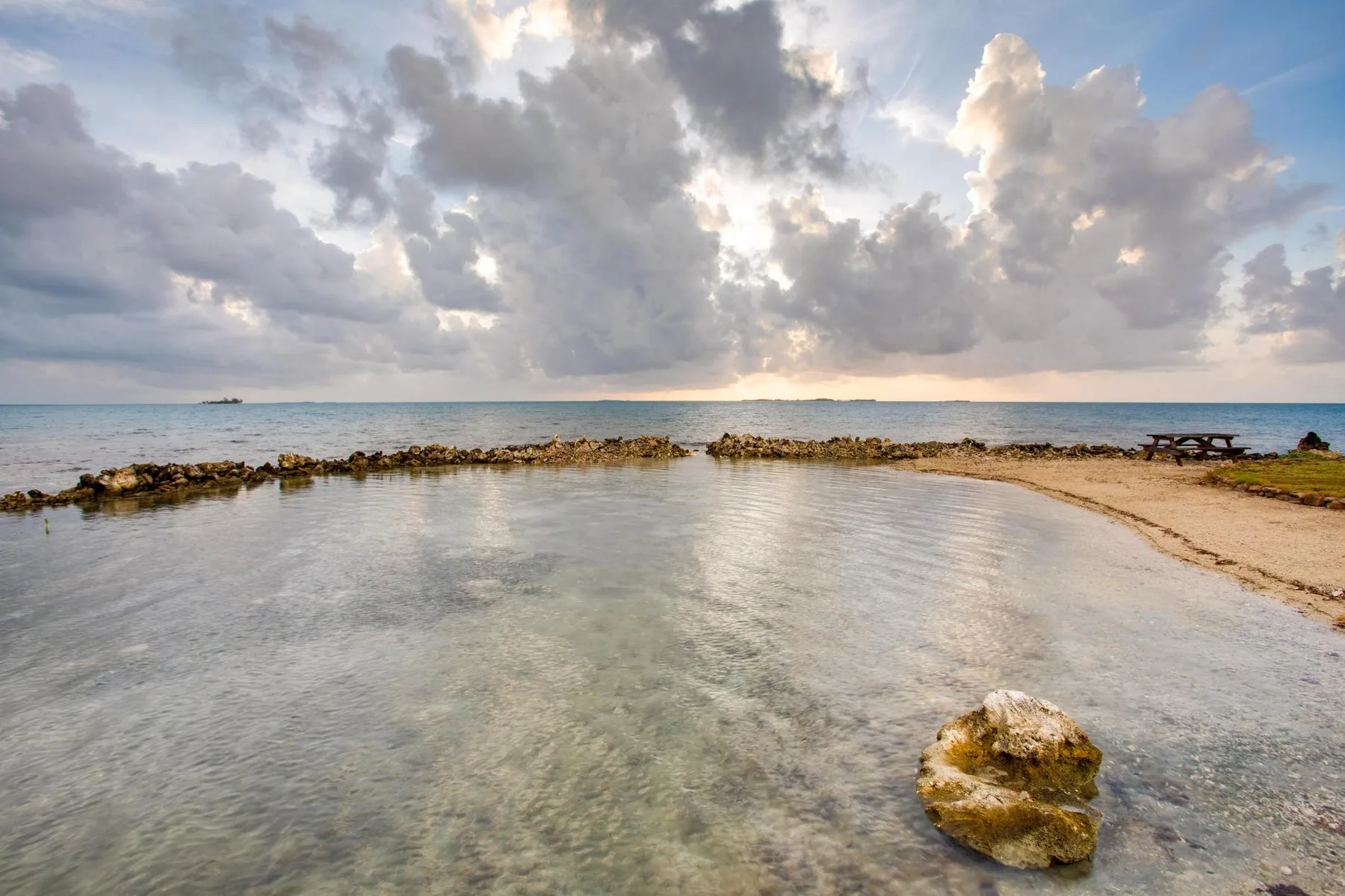 A shallow coastal lagoon lies beside a sandy beach under a cloudy sky.