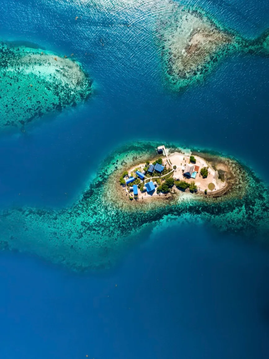 Aerial view of a small island surrounded by clear blue water and reef.