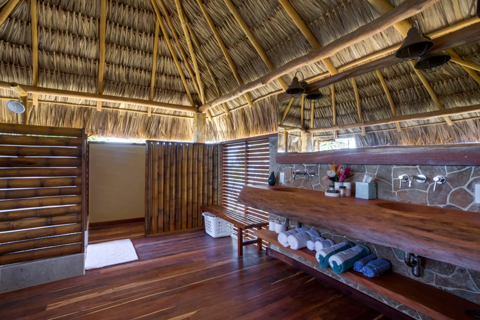 An open-air bathroom with a long wooden counter and thatched roof.