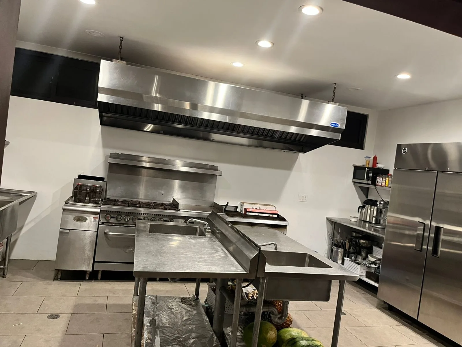 A commercial kitchen with stainless steel worktables and cooking equipment beneath a large ventilation hood.