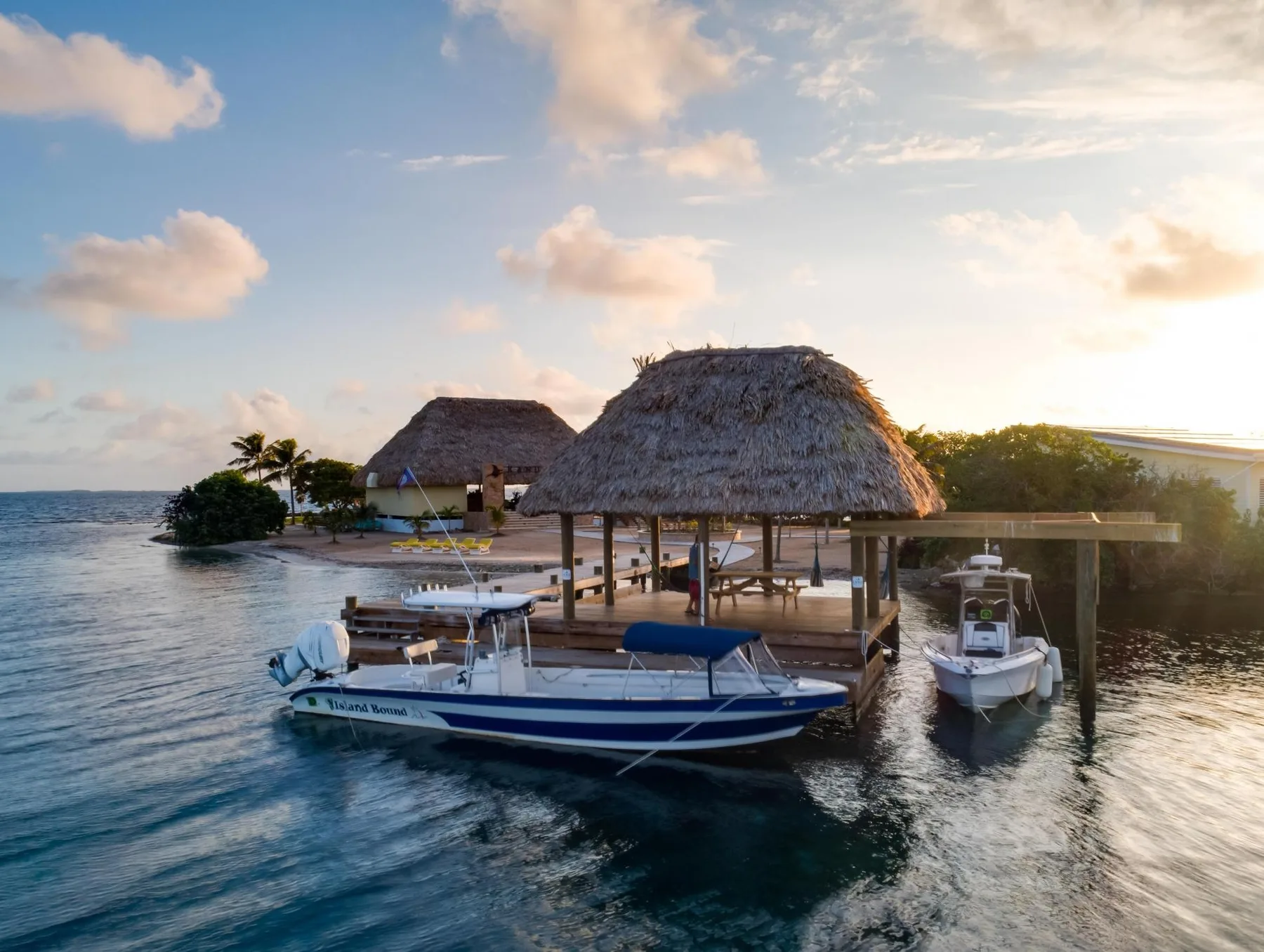 A thatched-roof pavilion stands over the water beside several moored boats.
