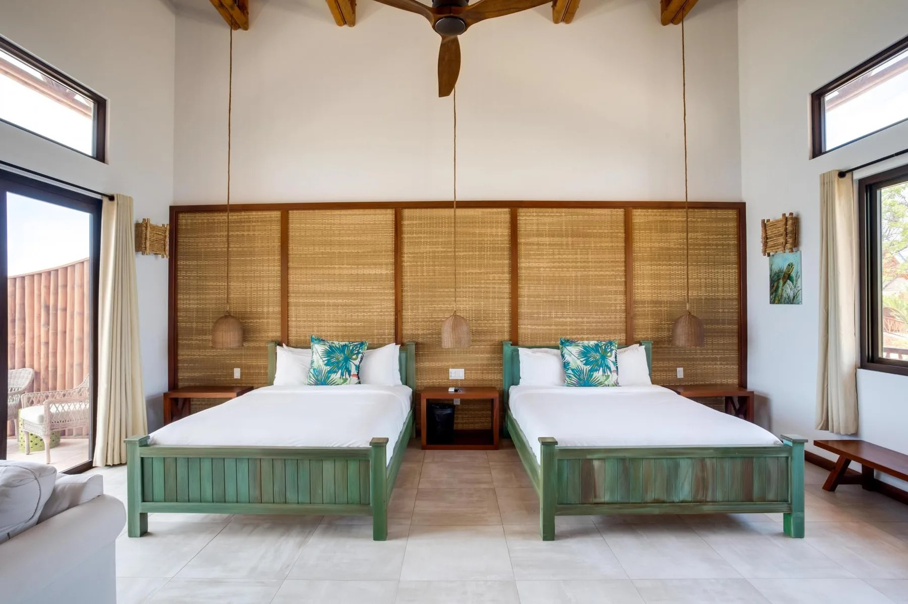 A bedroom with two beds, green frames, and a woven screen behind them.