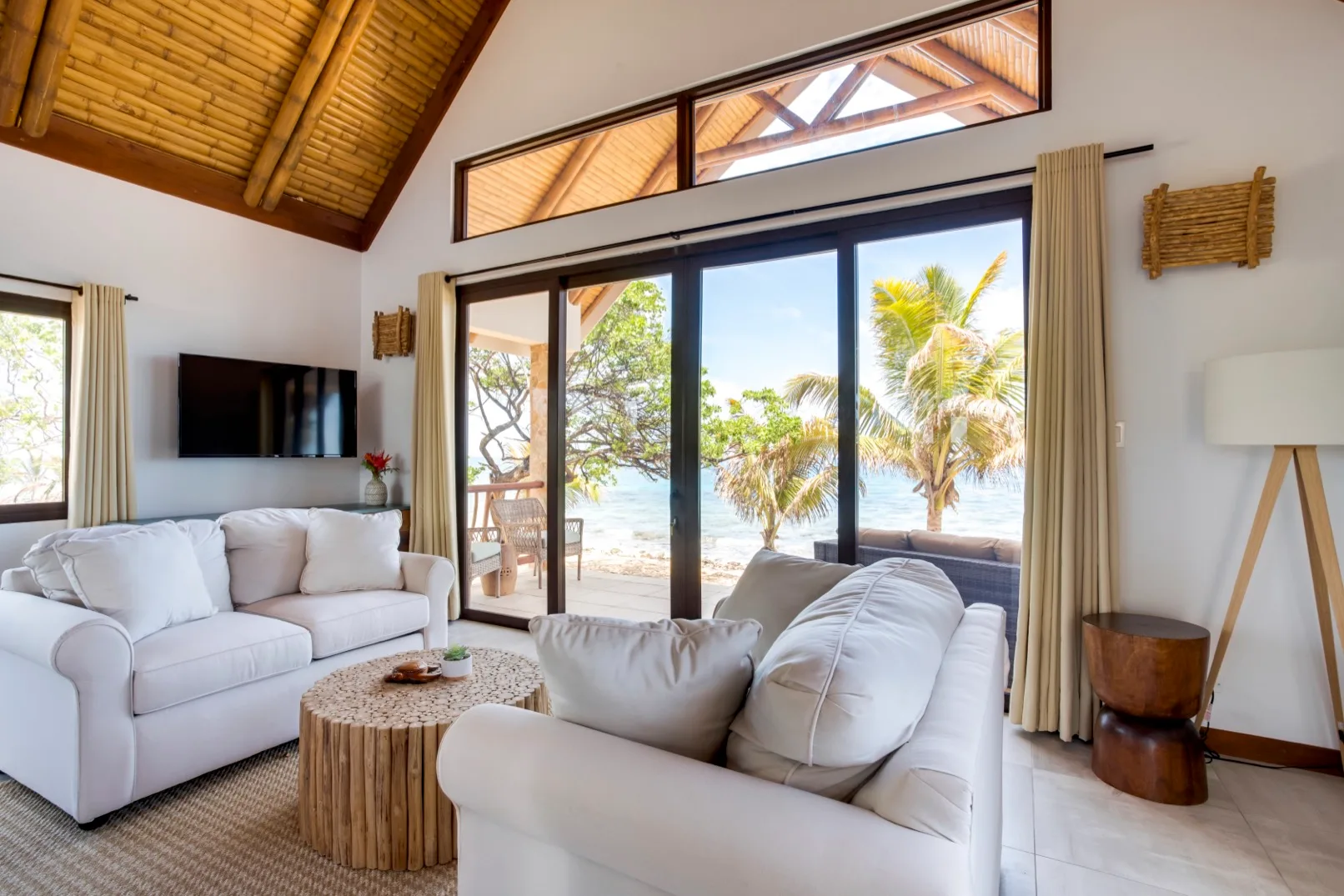 A bright living room with white seating and wide glass doors opening to a palm-lined view.