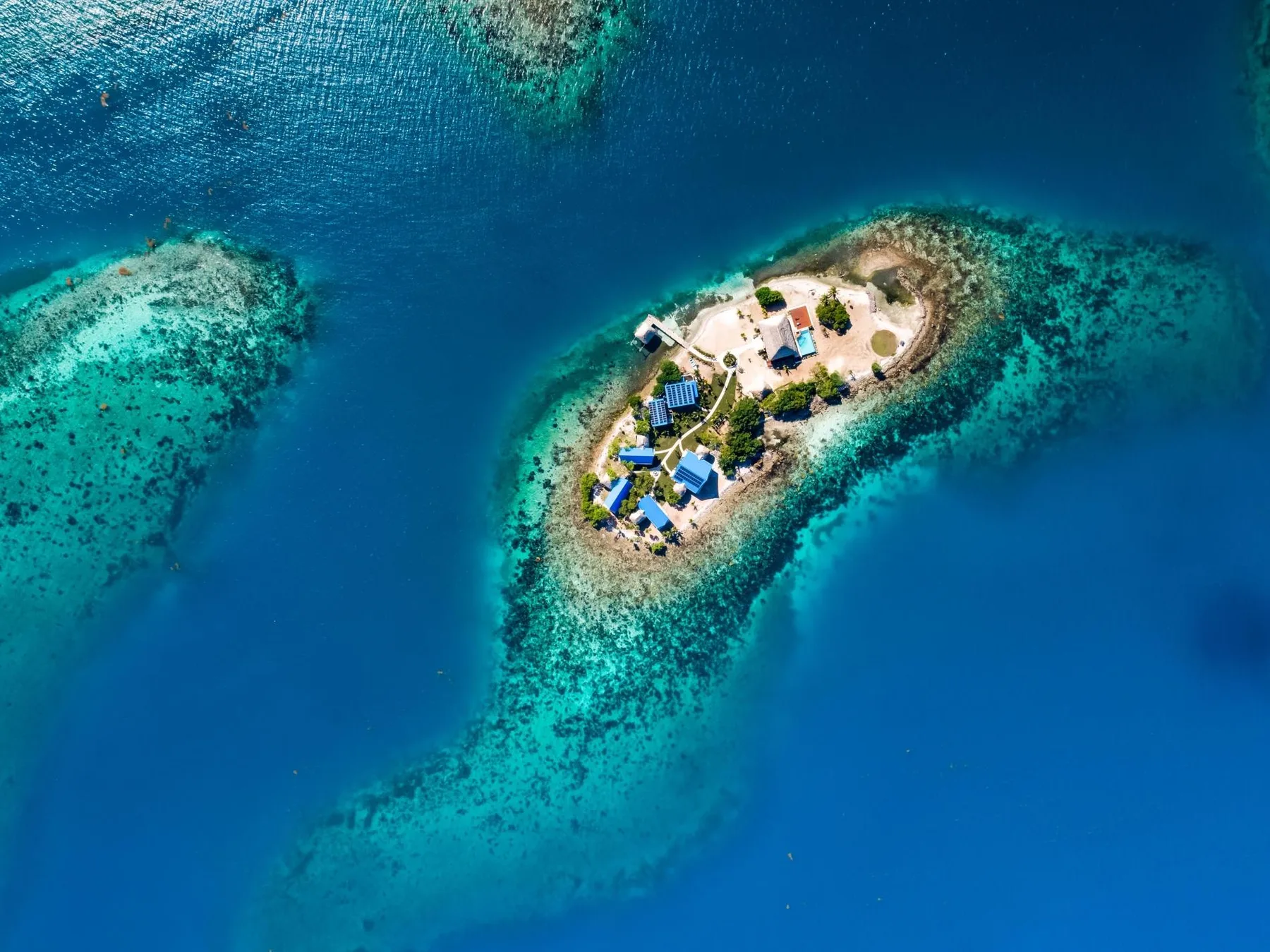 Aerial view of a small island surrounded by blue water and coral reefs.