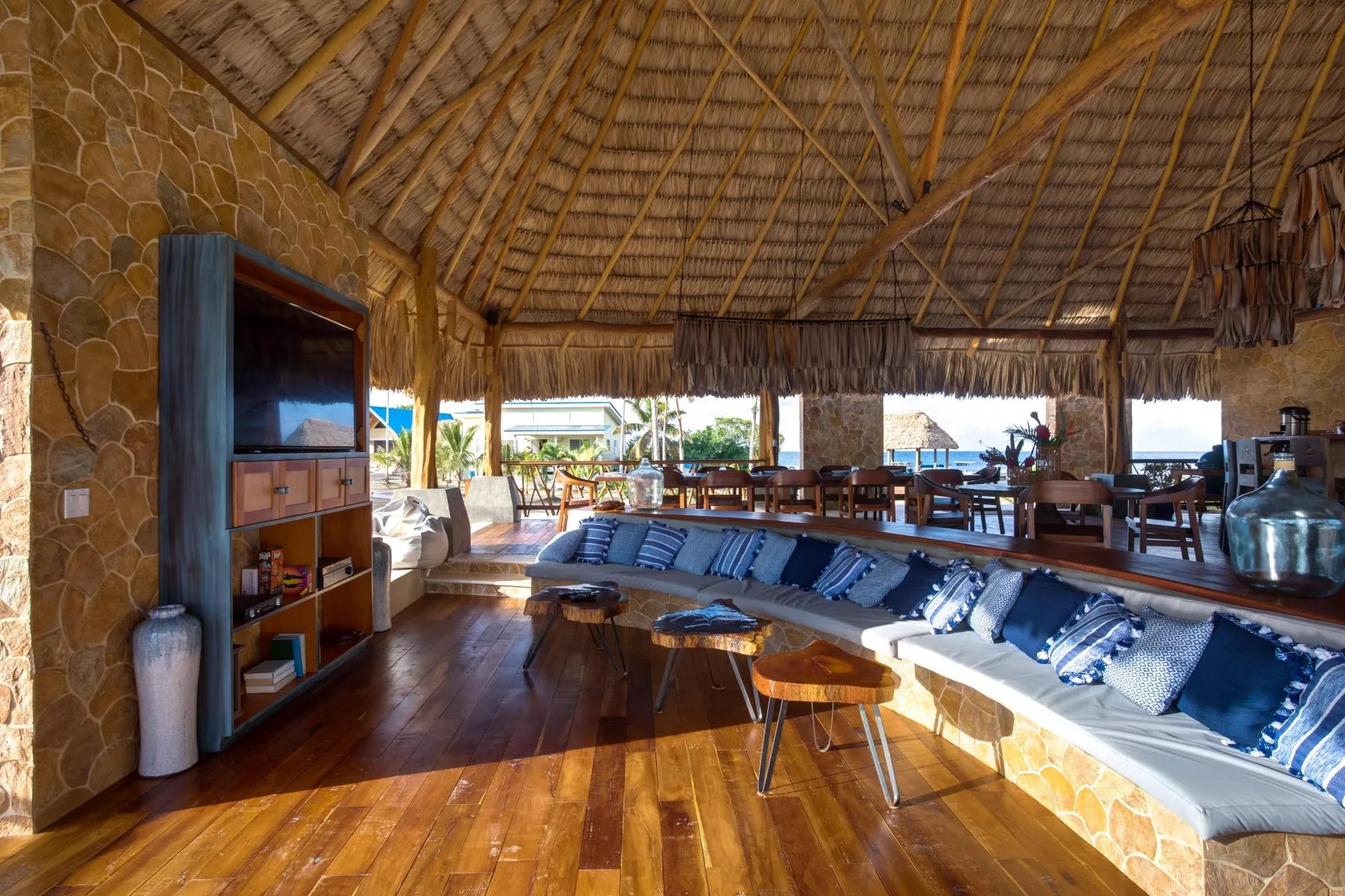 An open-air lounge with a long seating area beneath a thatched roof.