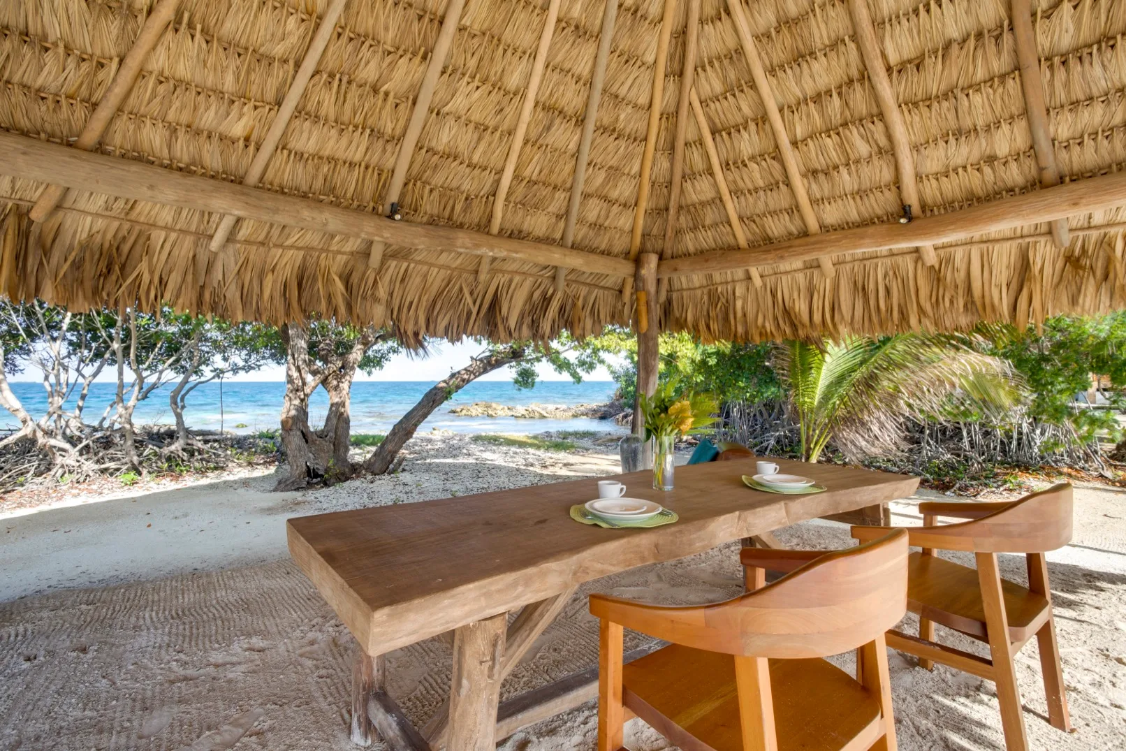 An open-air dining area beneath a thatched roof overlooks the beach.