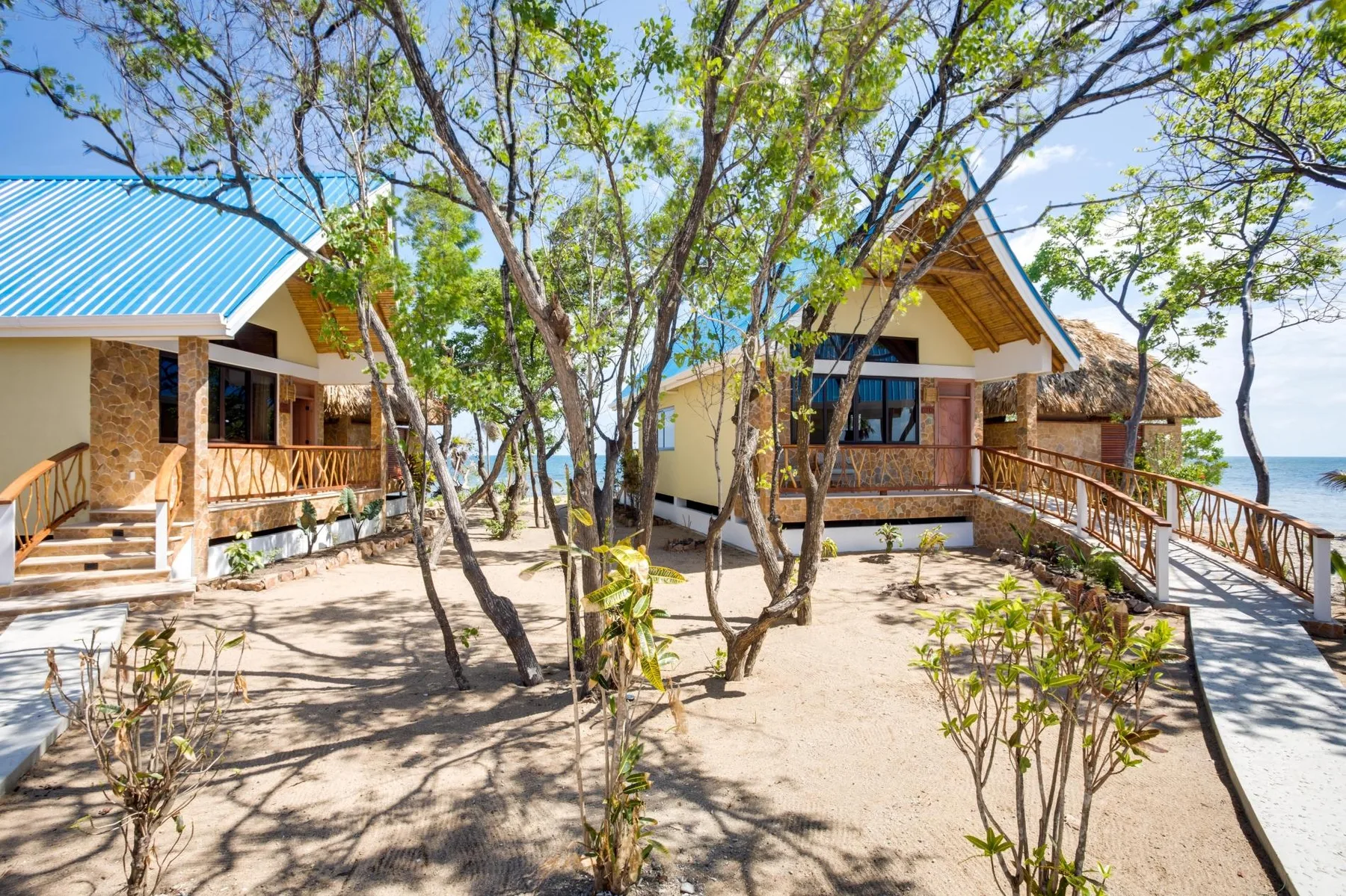 Beachside cottages stand among trees beside a sandy path and the water.