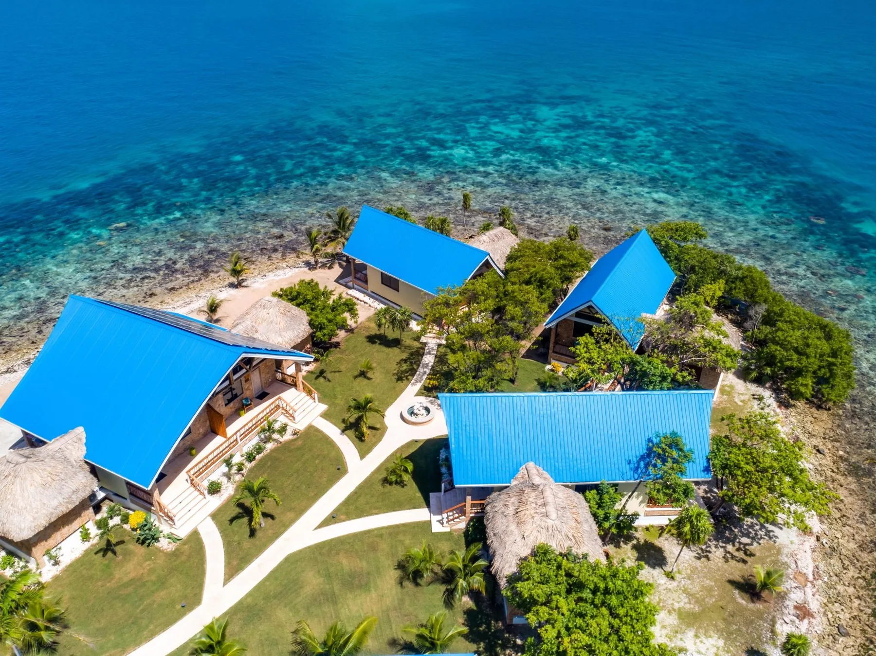 Aerial view of several blue-roofed buildings beside clear turquoise water.